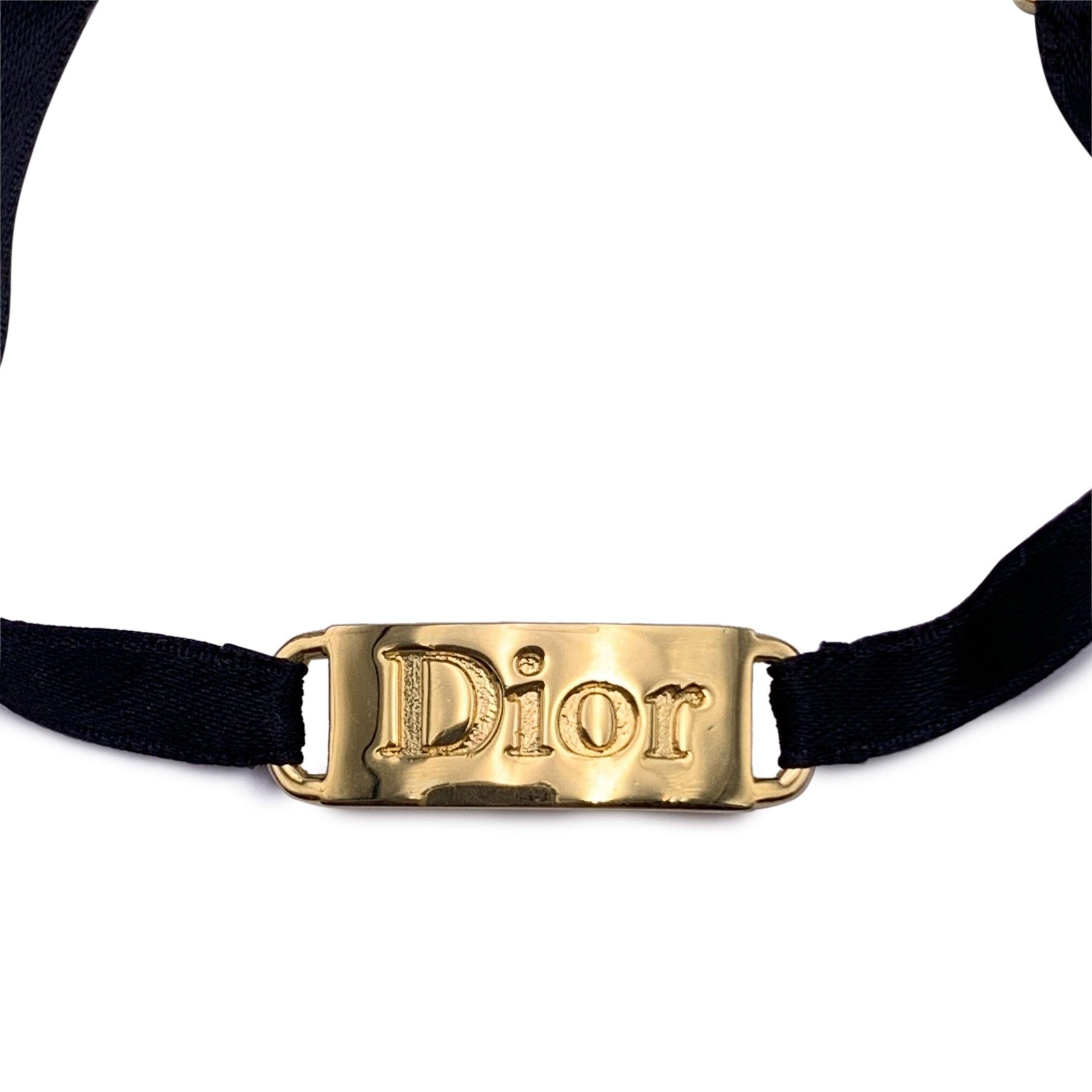 Vintage black satin ribbon bracelet by CHRISTIAN DIOR. Gold metal Dior logo plate element with rhinestones in the center. Lobster closure. Total lenght: 9 inches - 22.8 cm. 'Dior' engraved on the small CD charm at the end of the bracelet. Condition