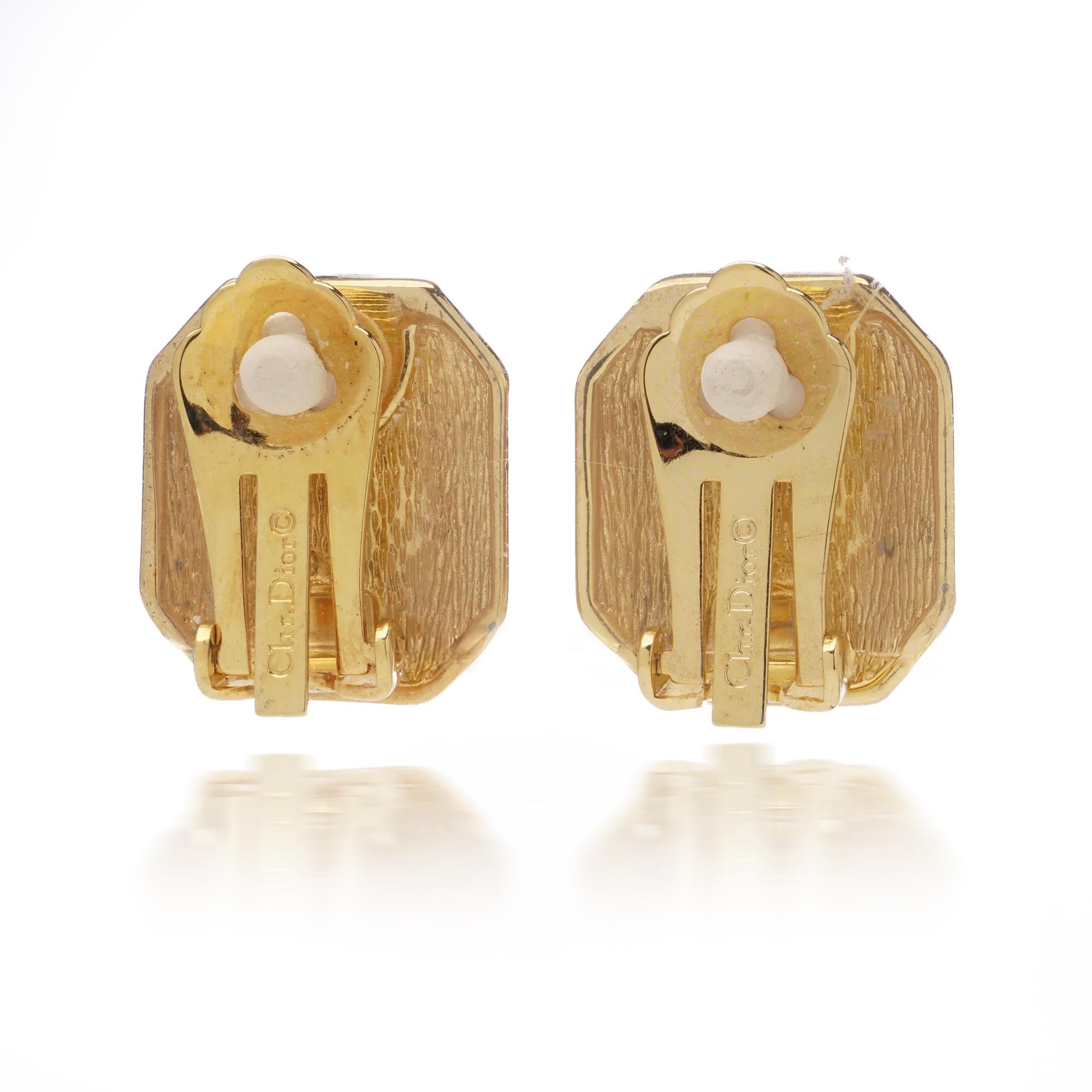 A striking pair of Christian Dior vintage gold-plated clip-on earrings, crafted in a bold octagonal design. Each earring features a deep blue emerald-cut glass stone at the centre, framed by a border of sparkling clear crystals that highlight the