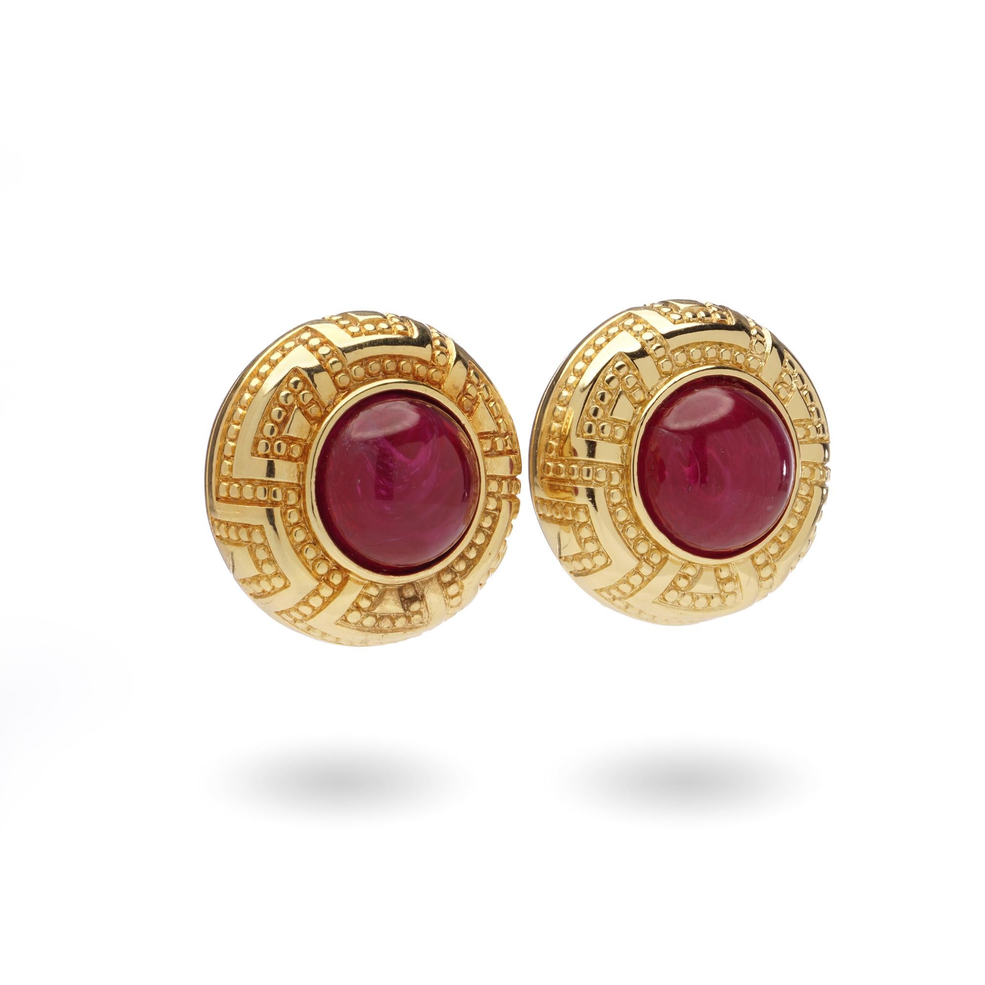 A striking pair of Christian Dior vintage clip-on earrings from the 1980s, designed in a bold circular form. Crafted in rich gold-tone metal, each earring is set with a vibrant ruby-red cabochon glass centre framed by textured detailing. With their