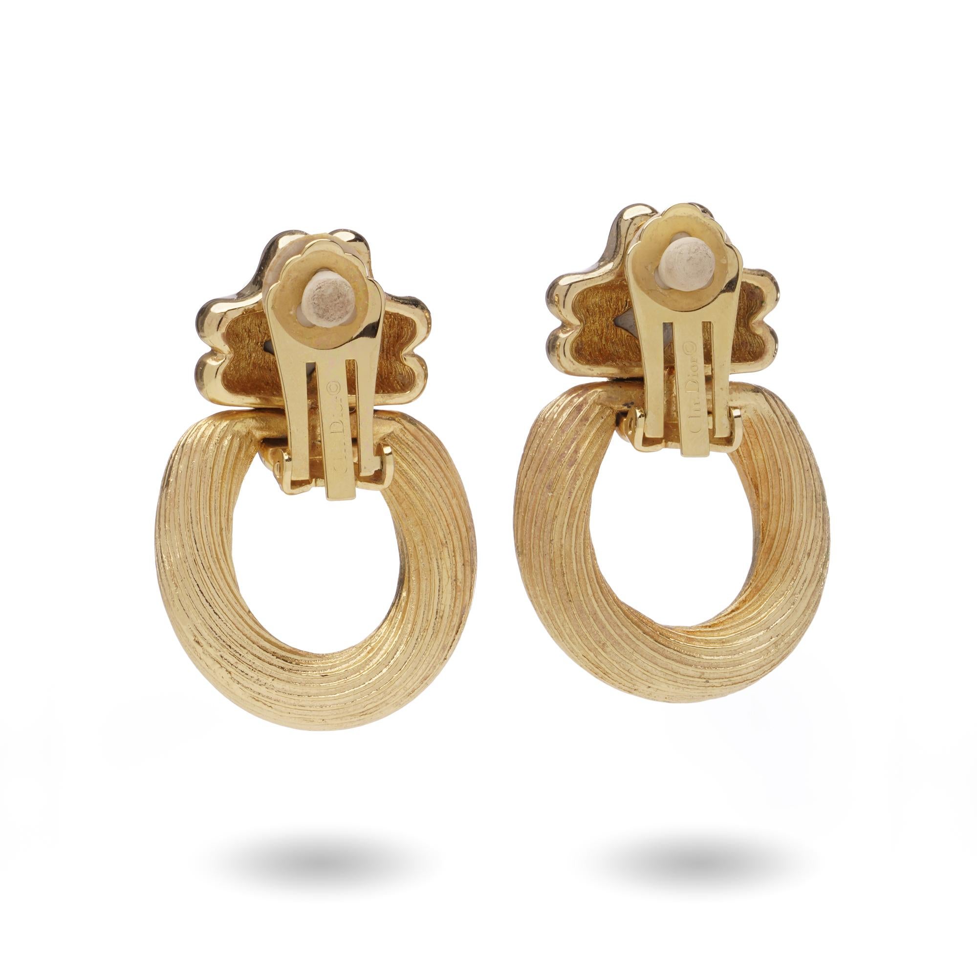 A striking pair of Christian Dior vintage clip-on earrings from the 1980s, crafted in a bold gold-tone design. The earrings feature textured hoop drops suspended from sculptural, stylised mounts, creating a chic statement look. Signed Dior to the