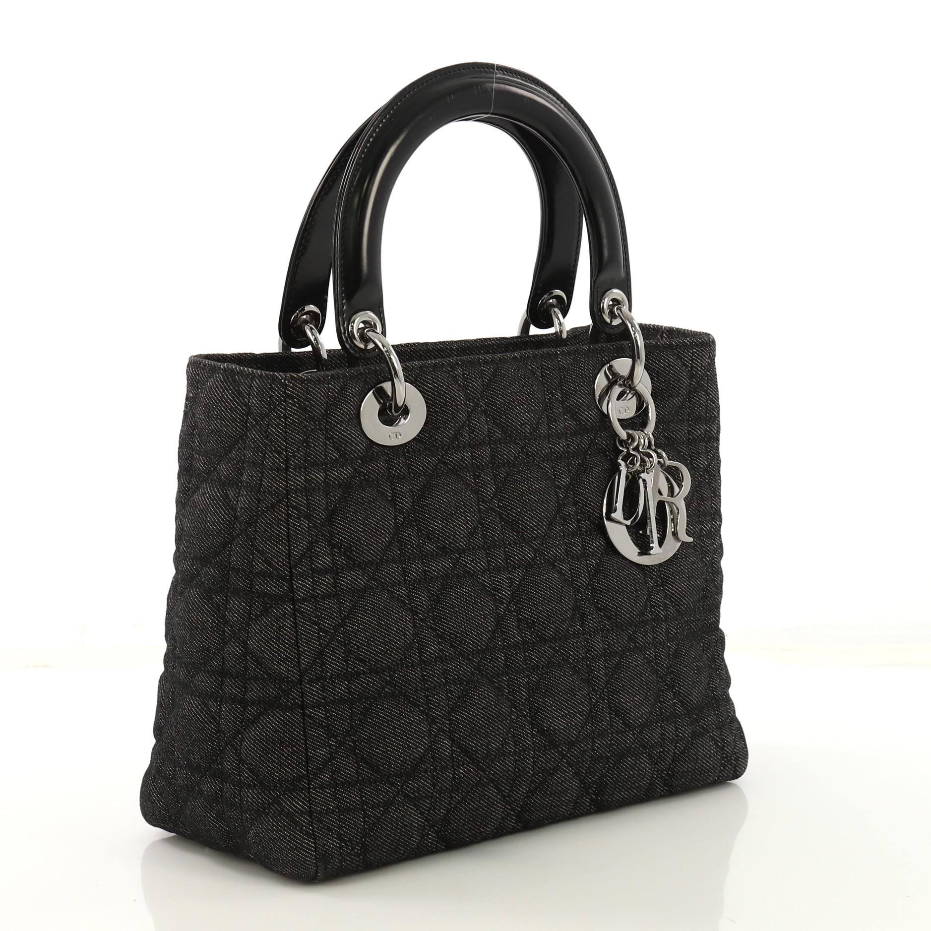 This Christian Dior Vintage Lady Dior Handbag Cannage Quilt Denim Medium, crafted in black quilted denim, features short dual handles with Dior charms and silver-tone hardware. Its top zip closure opens to a black fabric interior with zip pocket.