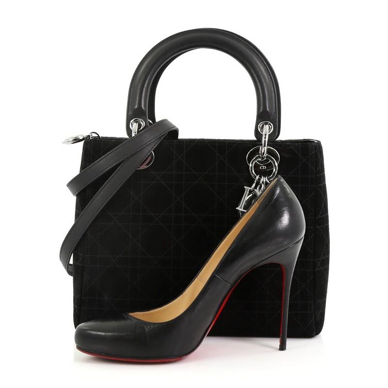 This Christian Dior Vintage Lady Dior Handbag Stitched Cannage Suede Medium, crafted in black stitched cannage suede, features dual top leather handles, Dior charms, protective base studs and silver-tone hardware. Its zip closure opens to a black