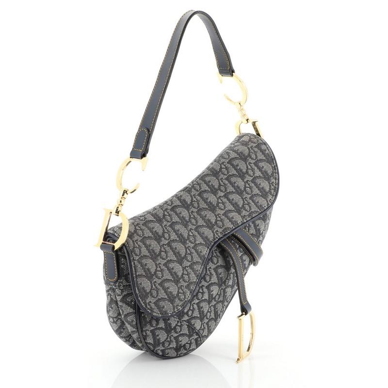 This Christian Dior Vintage Saddle Bag Diorissimo Canvas Medium, crafted from blue diorissimo canvas, features a top handle adorned with metal 'CD' finishing, saddle silhouette, and gold-tone hardware. Its fold over top opens to a printed fabric