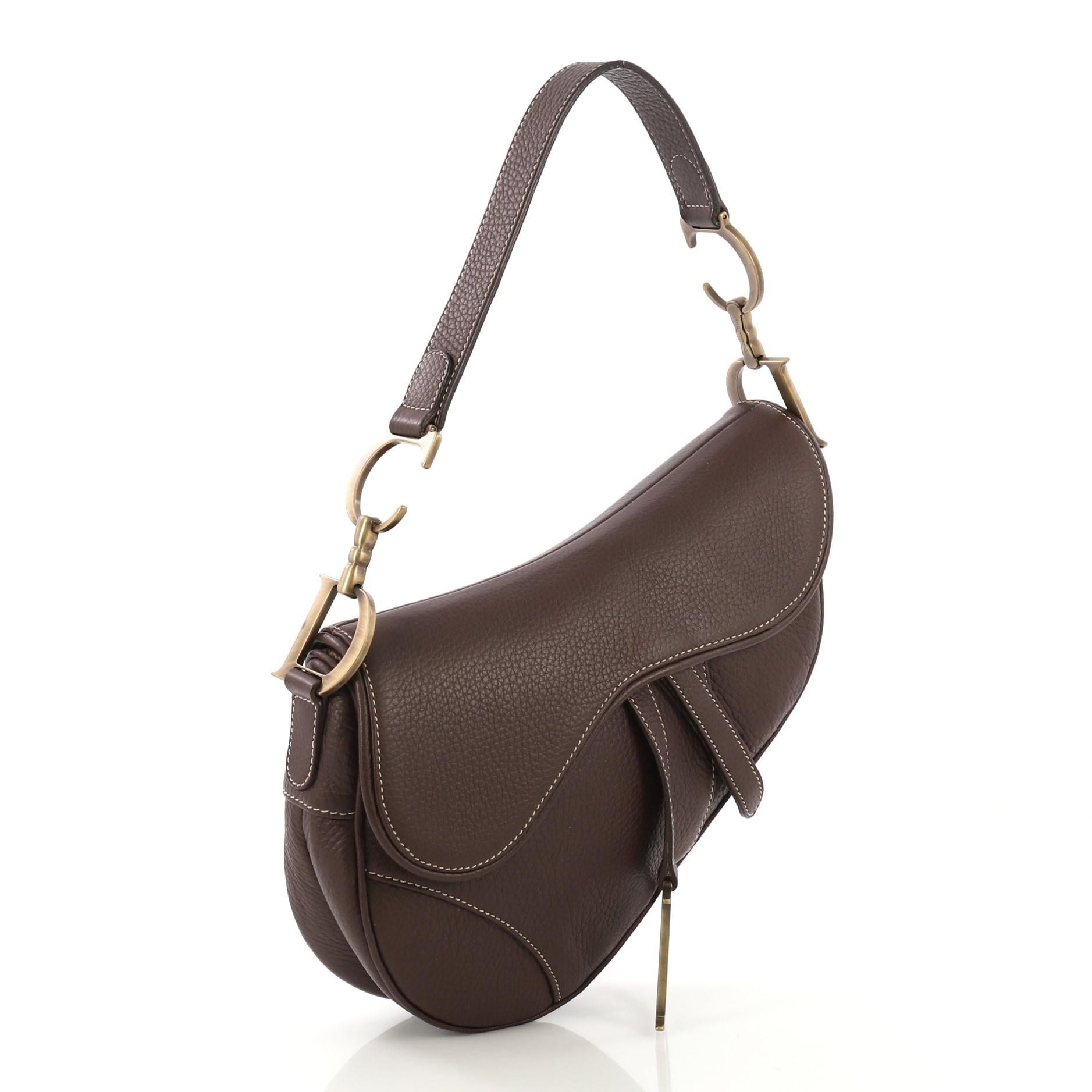 This Christian Dior Vintage Saddle Bag Leather Medium, crafted from brown leather, features a top handle adorned with metal 'CD' finishing, saddle-shaped silhouette, and aged gold-tone hardware. Its fold over top opens to a brown fabric interior