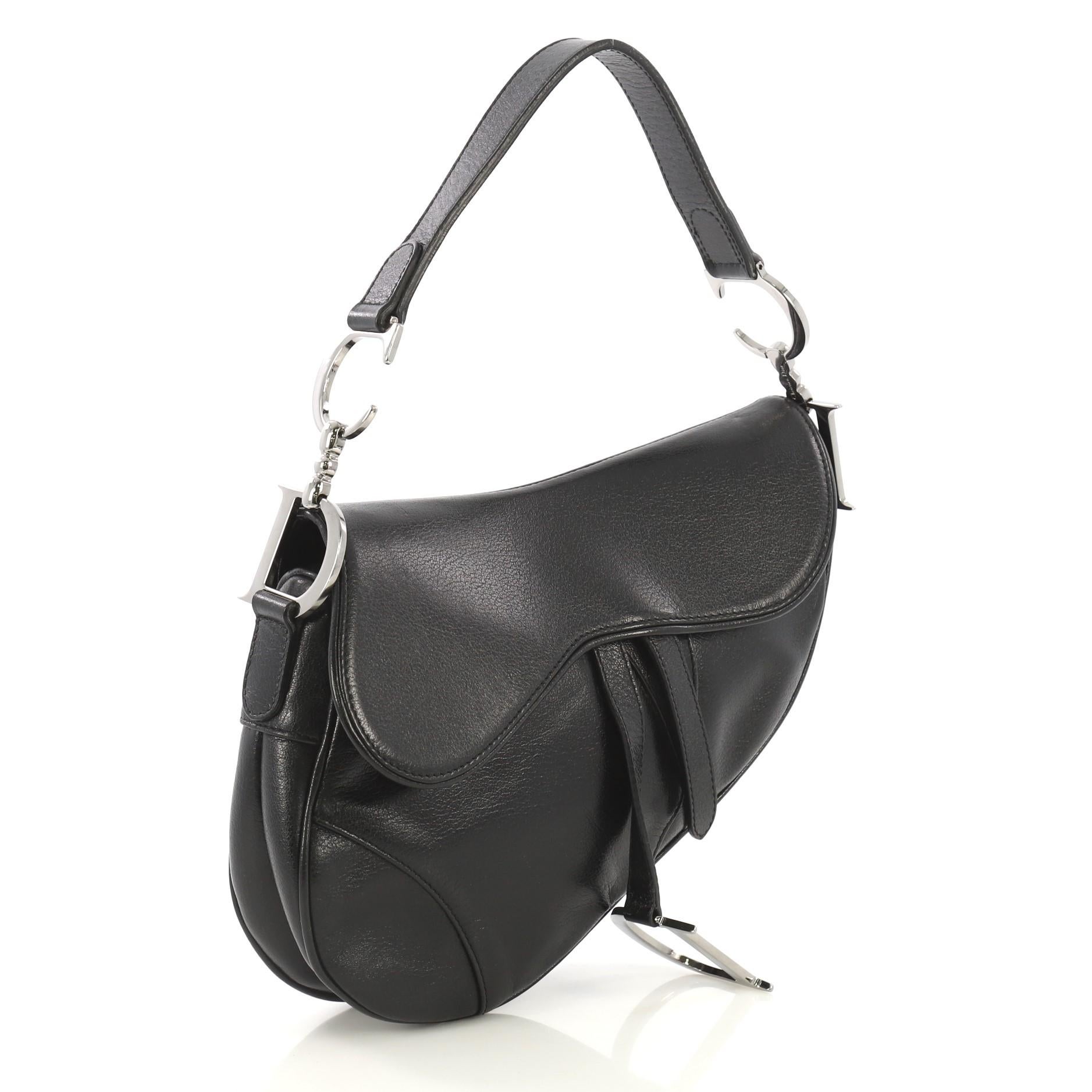 This Christian Dior Vintage Saddle Bag Leather Medium, crafted from black leather, features a top handle adorned with metal 'CD' finishing, saddle-shaped silhouette, and silver-tone hardware. Its fold over top opens to a black fabric interior with