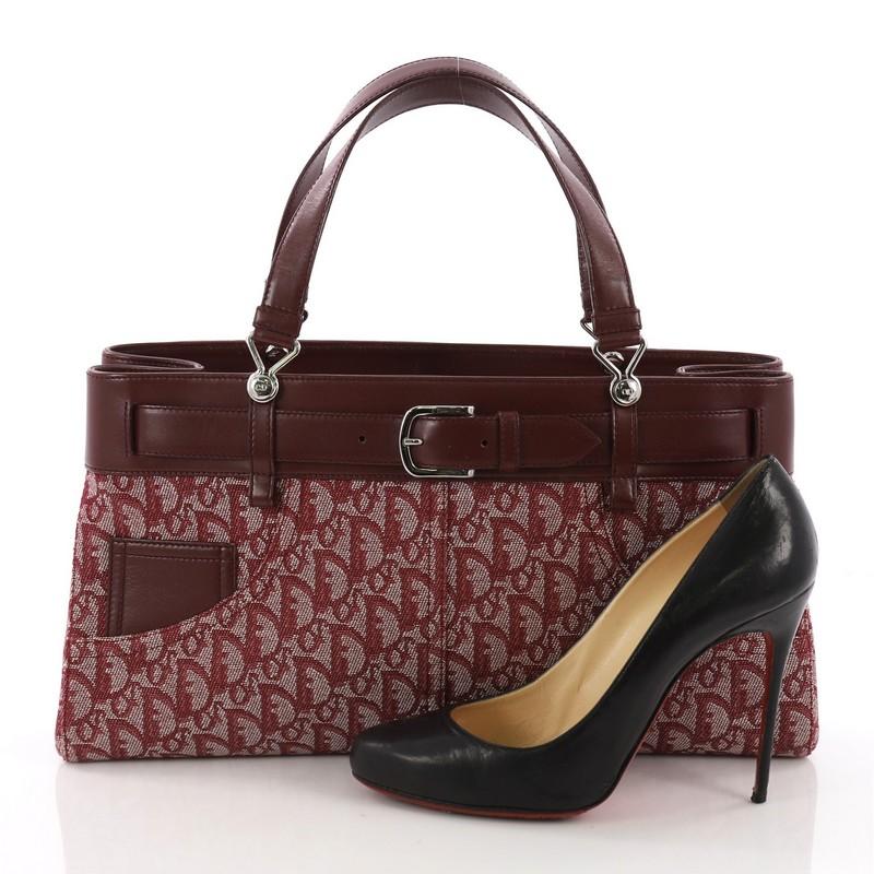 This Christian Dior Vintage Trotter Horizontal Tote Diorissimo Canvas Large, crafted from burgundy diorissimo canvas, features dual flat handles, front watch pocket, buckled sangles and silver-tone hardware. It opens to a plum fabric interior with