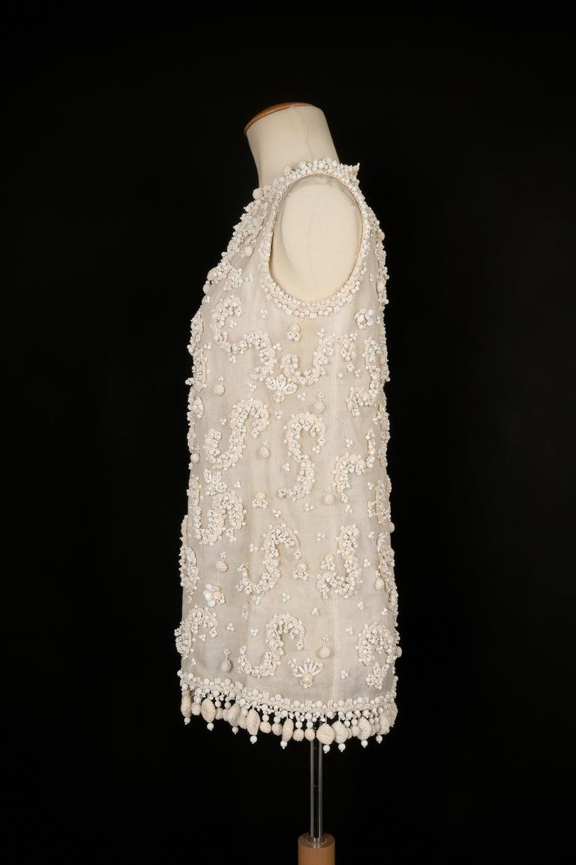 Dior - Cardigan en organdi de coton blanc entièrement brodé de pompons, de perles de guipure et de passementeries blanches. Aucune taille n'est indiquée, il convient à un 36FR. Collectional Printemps-Eté 1964 de la Haute Couture.

Informations