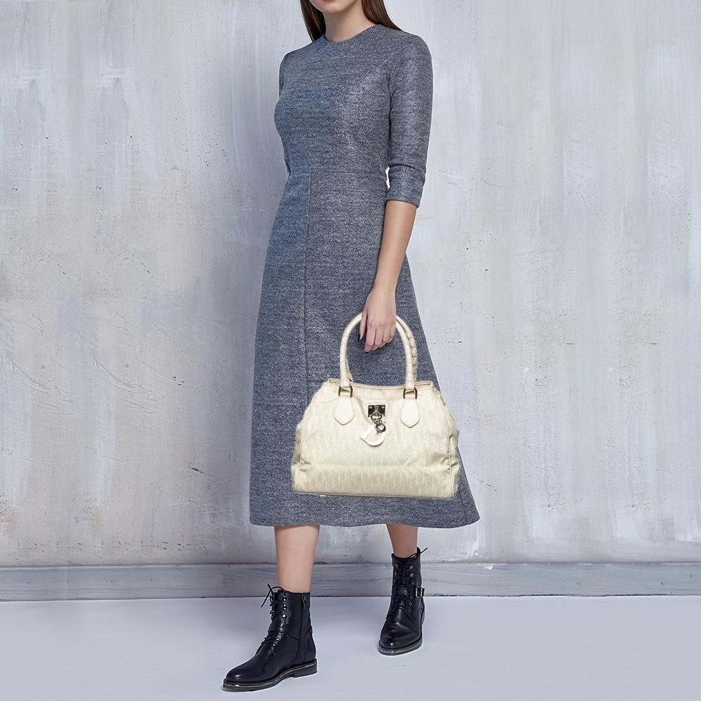 This Lovely tote from Christian Dior flaunts symbolic accents and details on its structure effortlessly. It is carved using white-cream canvas and leather on the exterior with silver-toned logo charms placed on the front. Accurate in its shape and