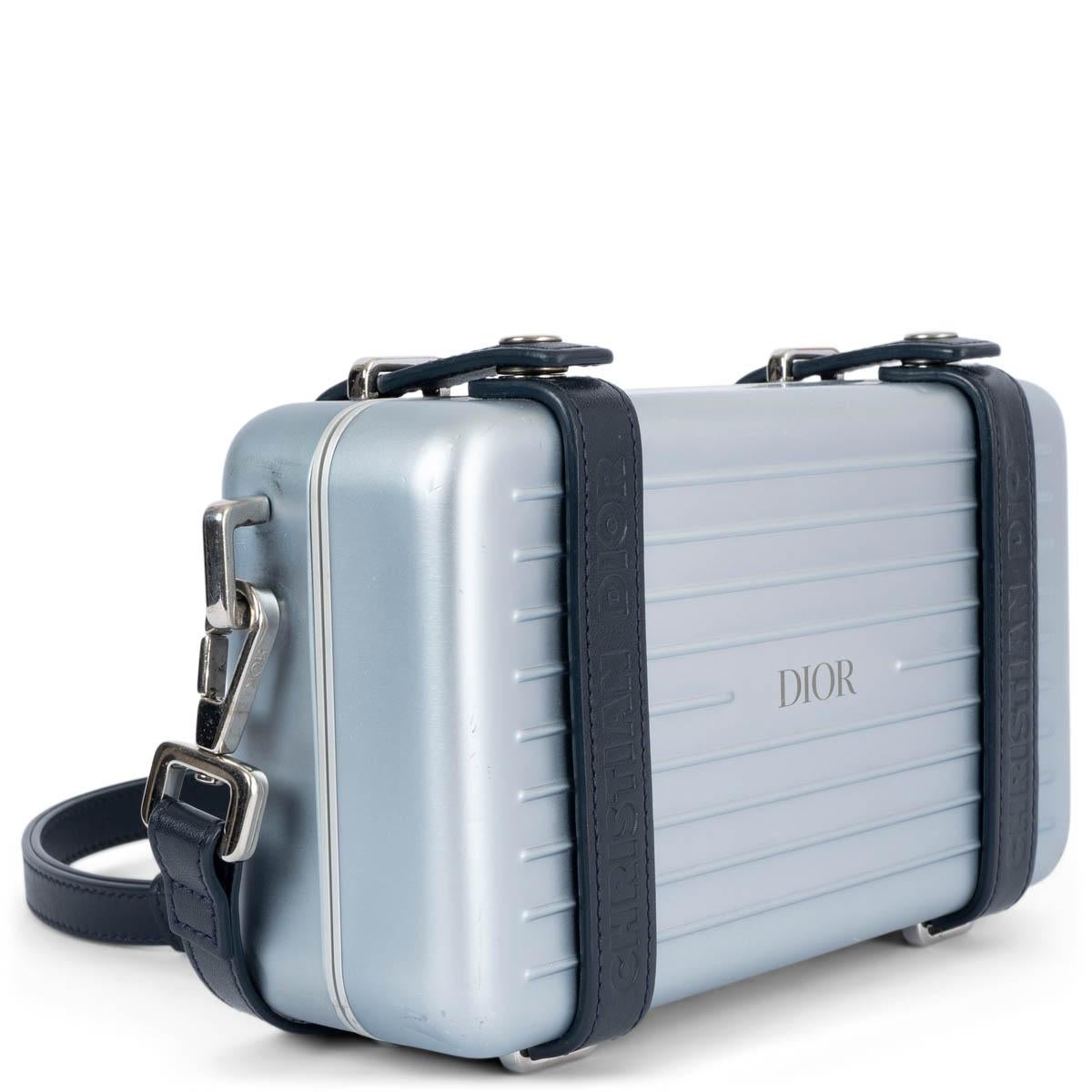 100% authentic Christian Dior x Rimowa 2022 Personal Clutch in metallic blue lightweight yet durable aluminum with dark blue leather trim and interior. Opens with push buttons to a interior divided in three compartment with one zipper pocket and six