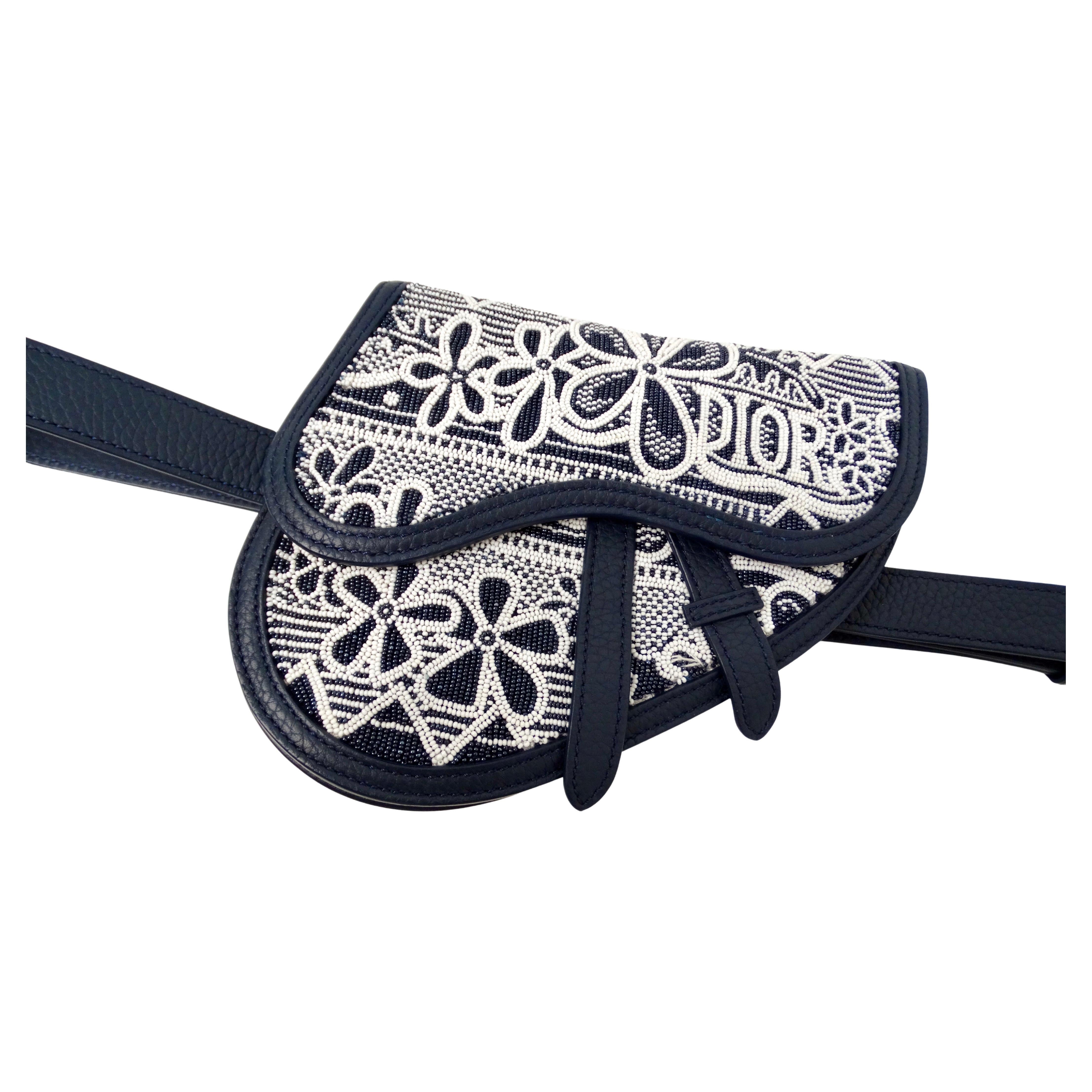 The Christian Dior x Shawn Stussy Navy Beaded Grained Calfskin Saddle Belt Bag is a striking fusion of high fashion and streetwear artistry. Crafted from luxurious grained calfskin in a deep navy hue, the bag features intricate beadwork with