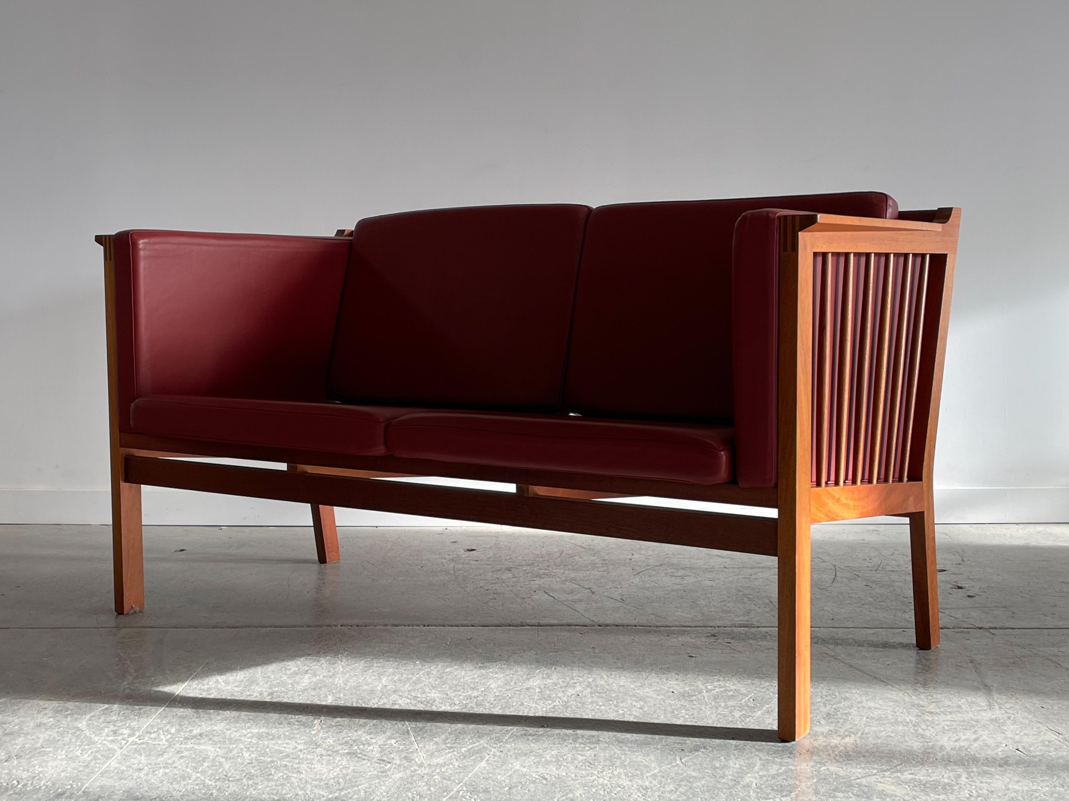 Simple and elegant. Mahogany and leather two seater sofa designed by Christian Hvidt for Soborg Mobler, Denmark. This piece features a beautiful spindle-back mahogany frame, angular armrests with box joinery, and oxblood leather cushions. Measures
