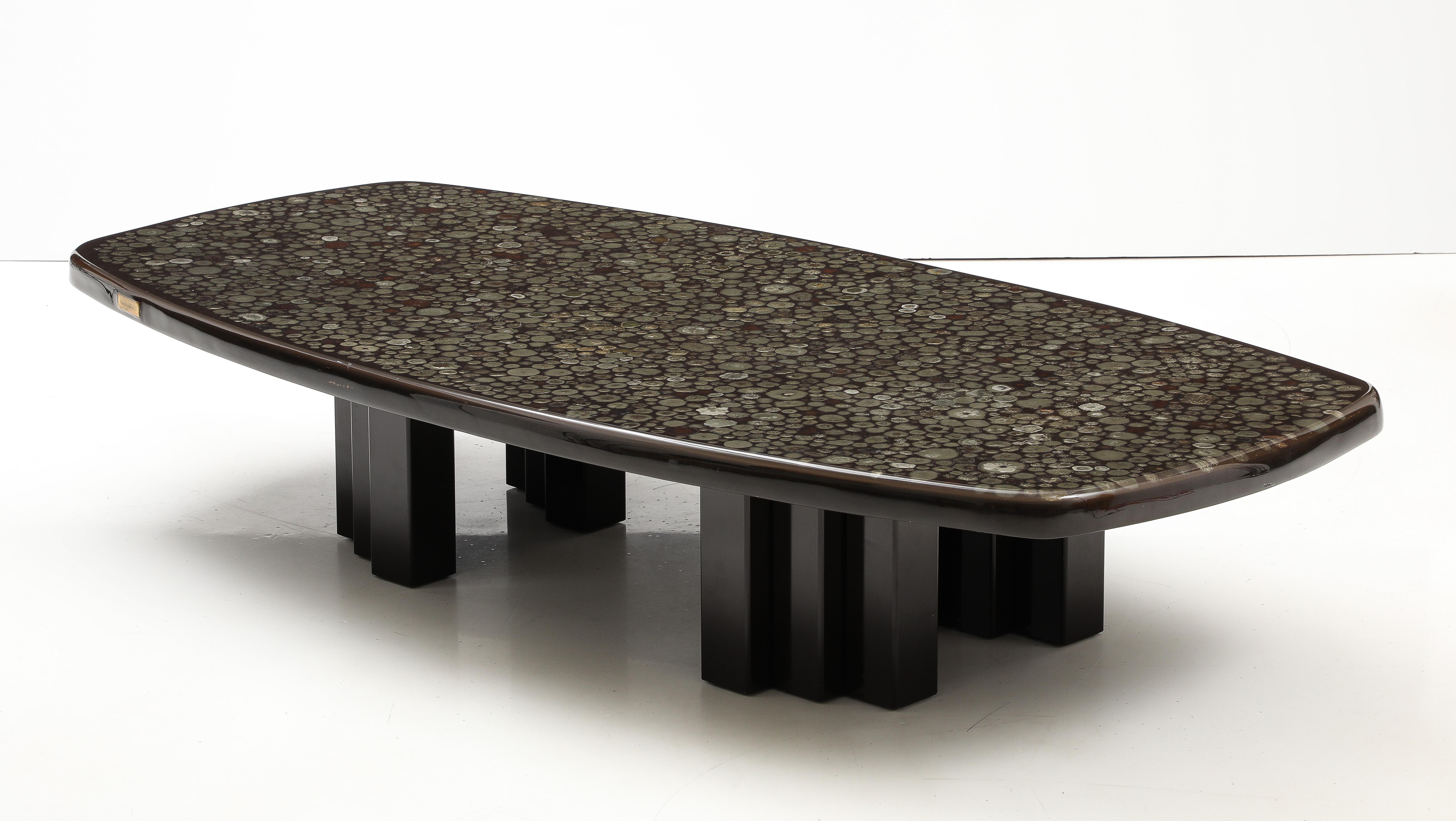 Voici une magnifique table basse de Christian Krekels, de forme oblongue, composée d'un plateau en résine incrusté de sections transversales de pyrite minérale, surmonté d'une base en acier émaillé brun-noir, chaque pied étant muni de trois supports