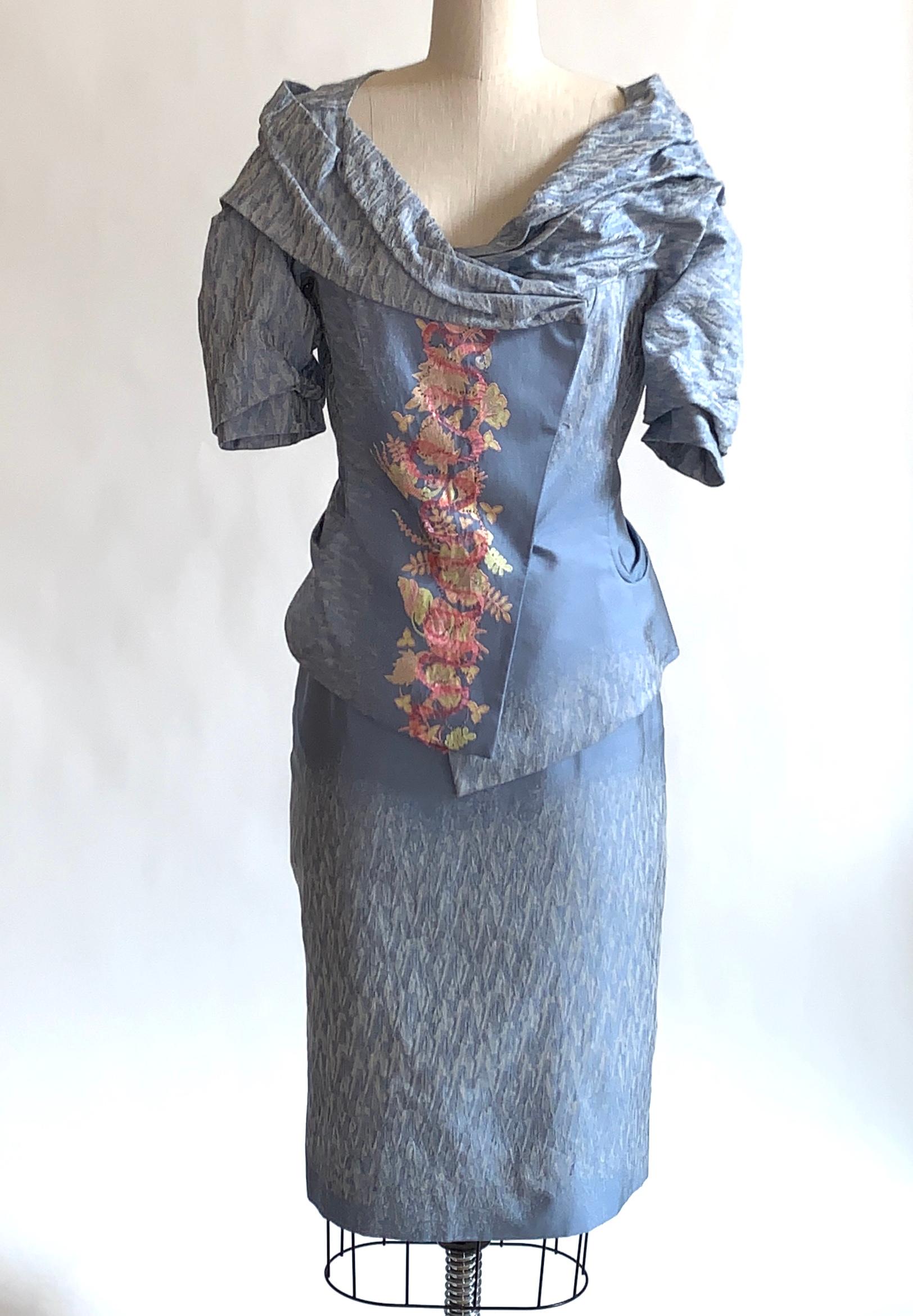 Vintage Christian Lacroix light blue skirt suit in an amazing textured jacquard fabric. Jacket features a portrait collar and slightly asymmetrical styling at hem with pink and yellow floral pattern and  pink ribbon appliqué at front. Snaps closed.