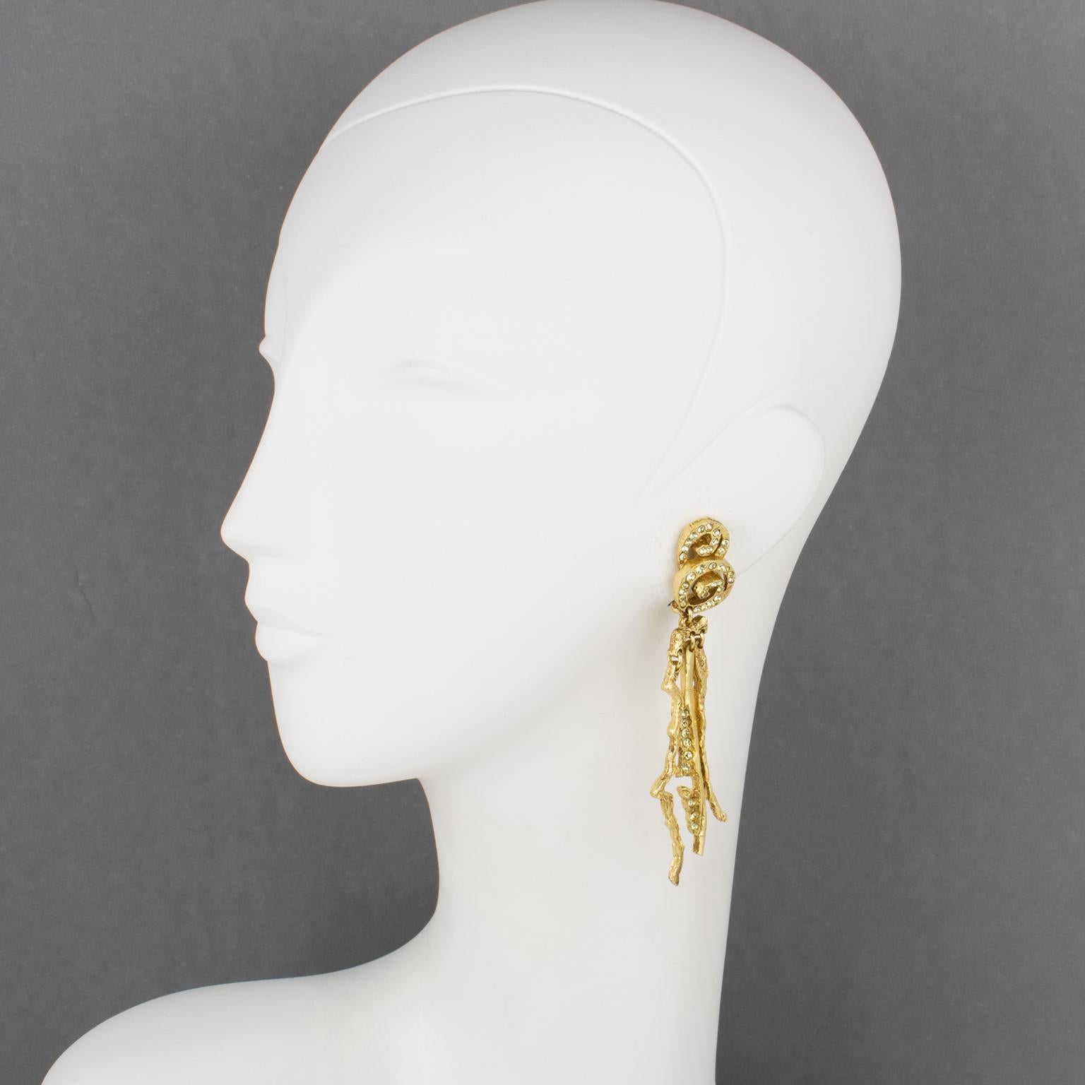 These superb Christian Lacroix Paris futuristic clip-on earrings feature a long dimensional brutalist dangling shape, with gilded metal all carved, textured, and see-thru, complimented with yellow champagne crystal rhinestones. Each piece is
