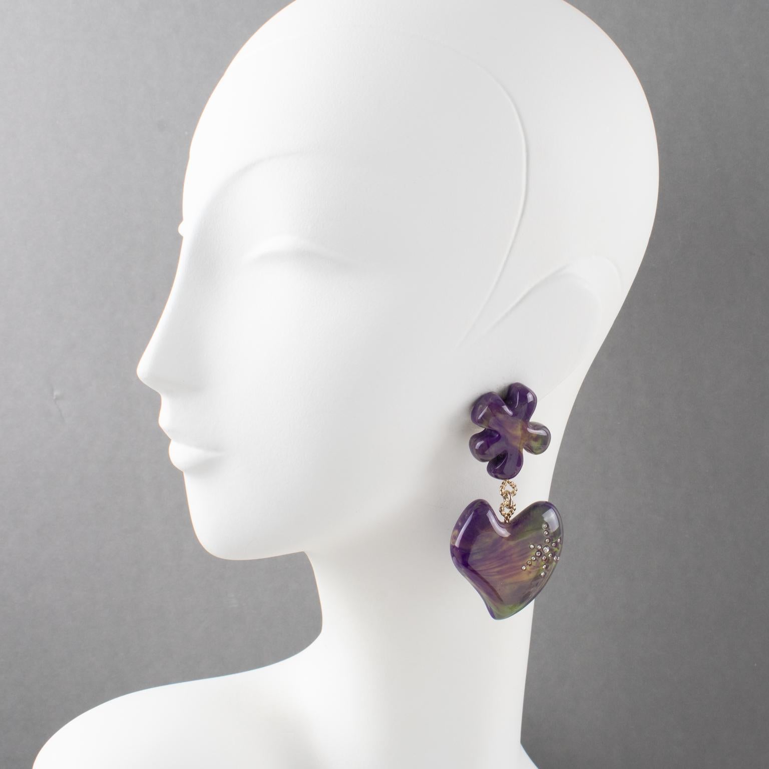 These gorgeous Christian Lacroix Paris signed clip-on earrings feature an oversized resin dangling shape with an abstract flower and heart ornate with clear crystal rhinestones. The pieces boast amethyst purple and wisteria purple, with bright