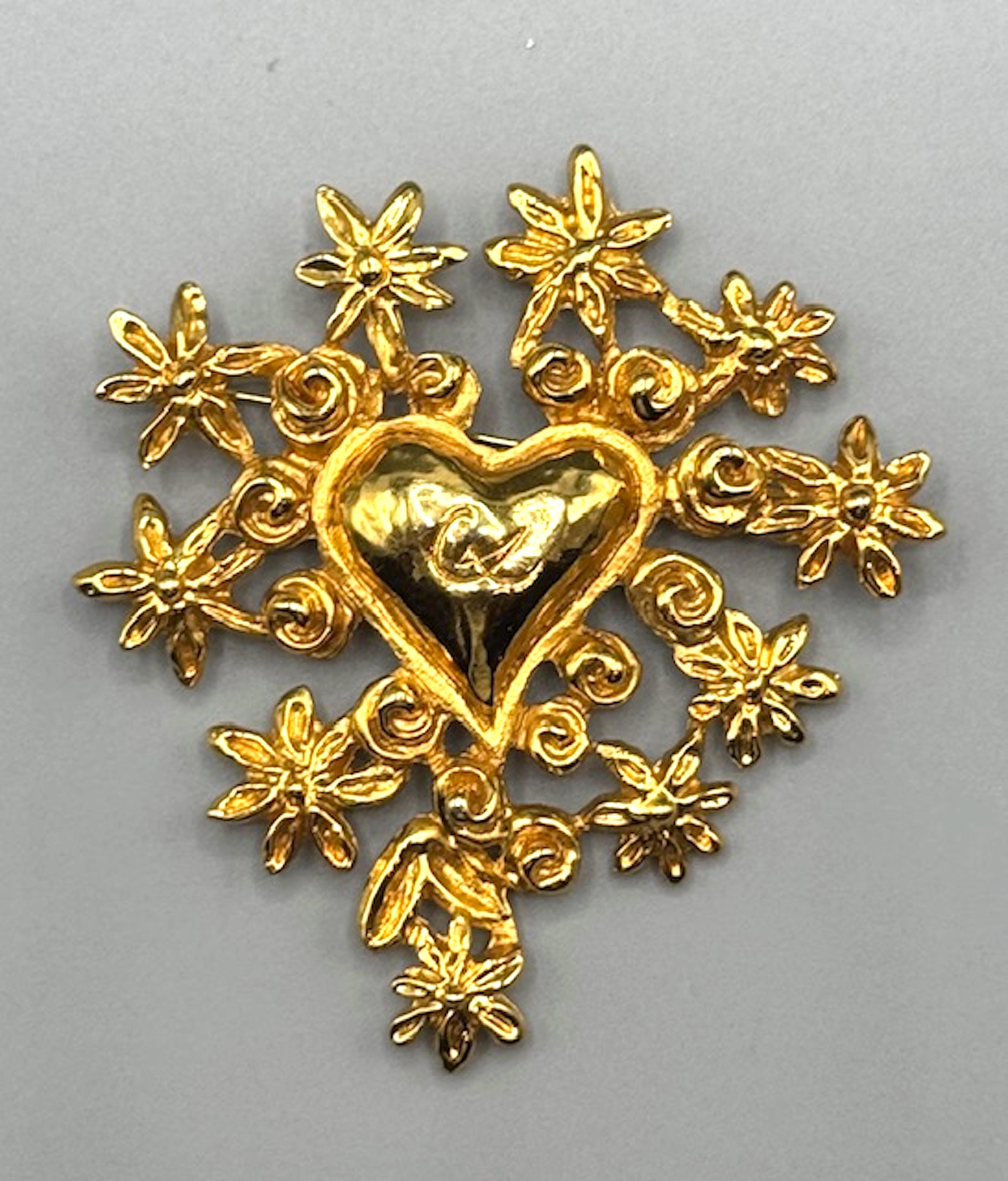 The Christian Lacroix “Noël 1993” brooch is a limited edition piece crafted for the 1993 Christmas collection. This gold-plated brooch features a central heart adorned with the iconic “CL” initials, encircled by seven petal-like flowers, embodying