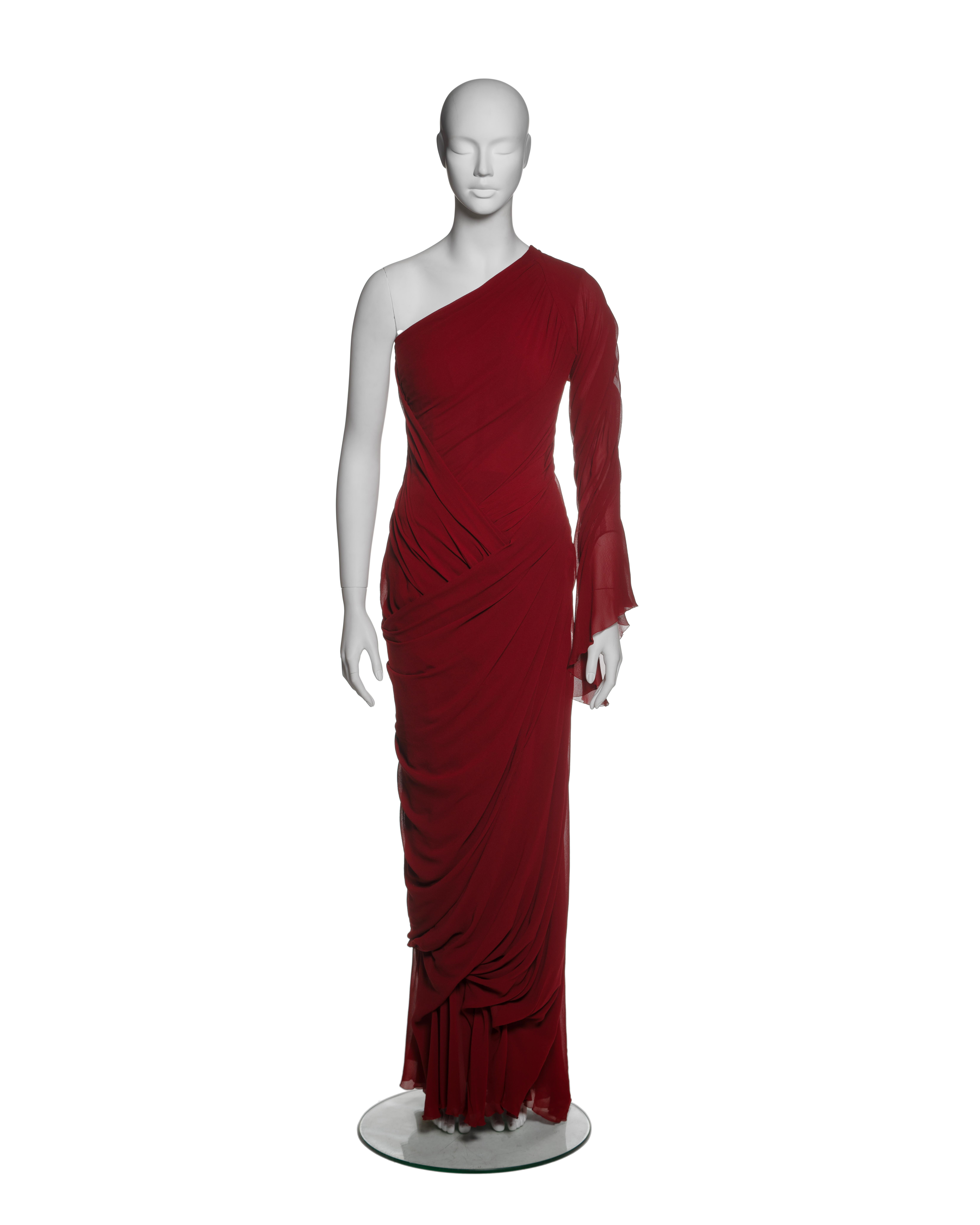 This Christian Lacroix dress from the Fall-Winter 1999 haute couture collection is an asymmetrical masterpiece crafted in rich crimson silk chiffon. The one-shoulder design features delicate draping across the bodice and a fitted silhouette that