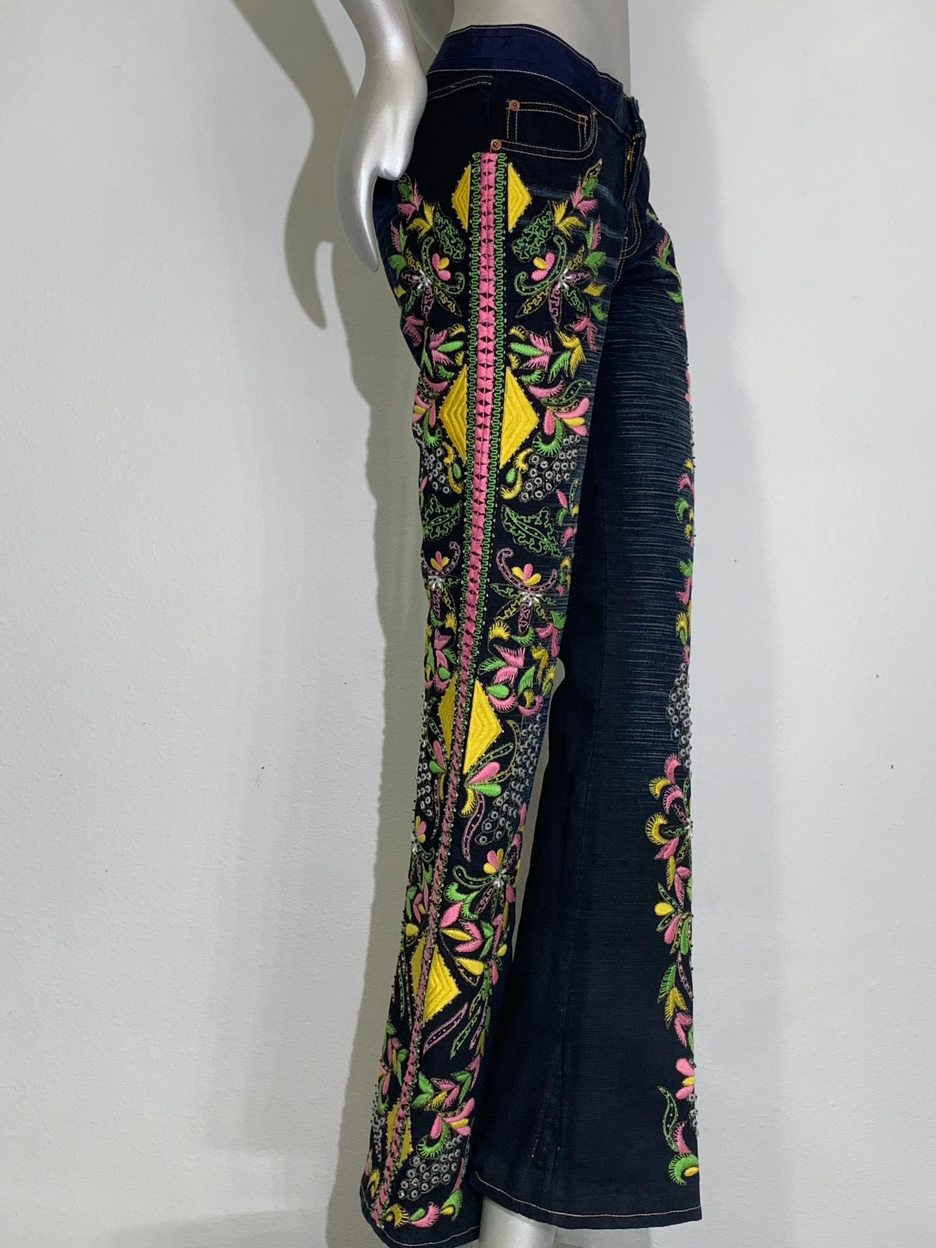 Pantalón vaquero Christian Lacroix en denim desgastado con bordados y abalorios: Los motivos geométricos y florales están bordados en tonos amarillo, chartreuse, rosa y lavanda, con un detalle de lazo bordado en el lateral. Cristales transparentes y