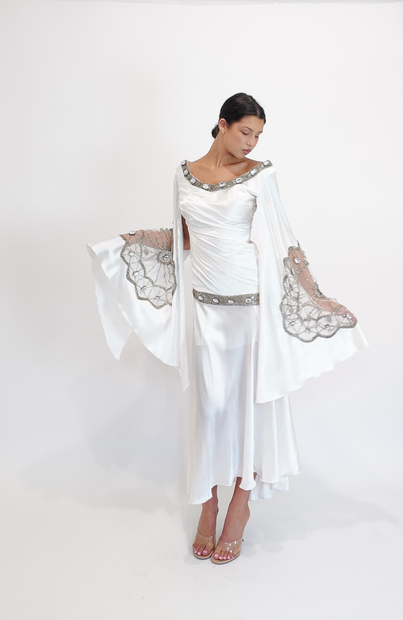 Dieses weiße Kleid von Christian Lacroix besticht durch exquisite Spitzenverzierungen und zarte Juwelen, die seinen eleganten Charme unterstreichen. Die Engelsärmel und die dezenten Rüschen sorgen für eine raffinierte Silhouette, während das