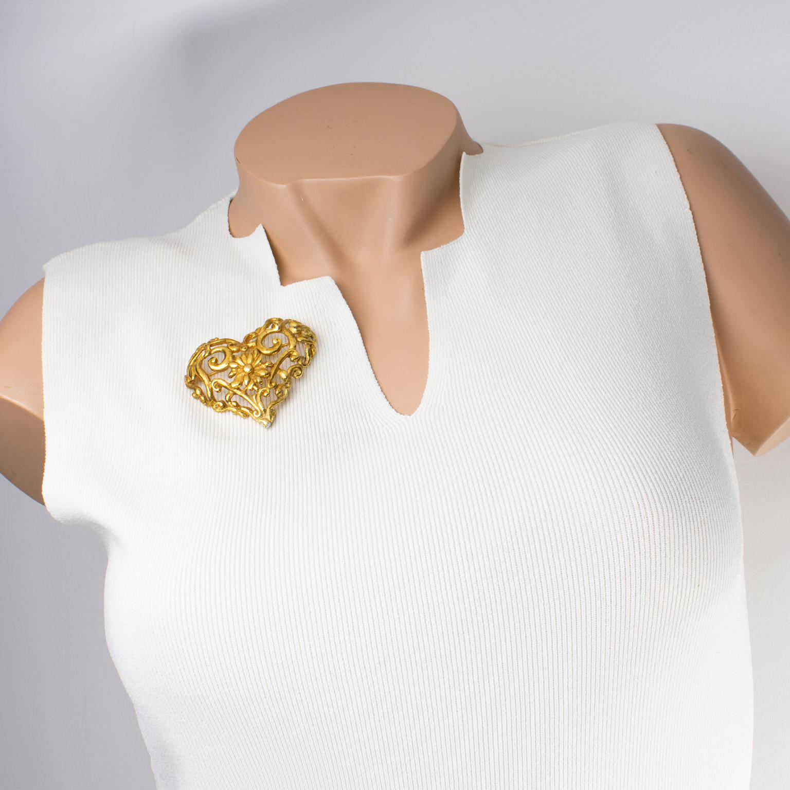 Christian Lacroix Paris a conçu cette superbe broche en forme de cœur baroque. Le design romantique présente un cœur dimensionnel en métal doré, entièrement sculpté et transparent, avec des fleurs, des arabesques et des volutes. La broche porte le