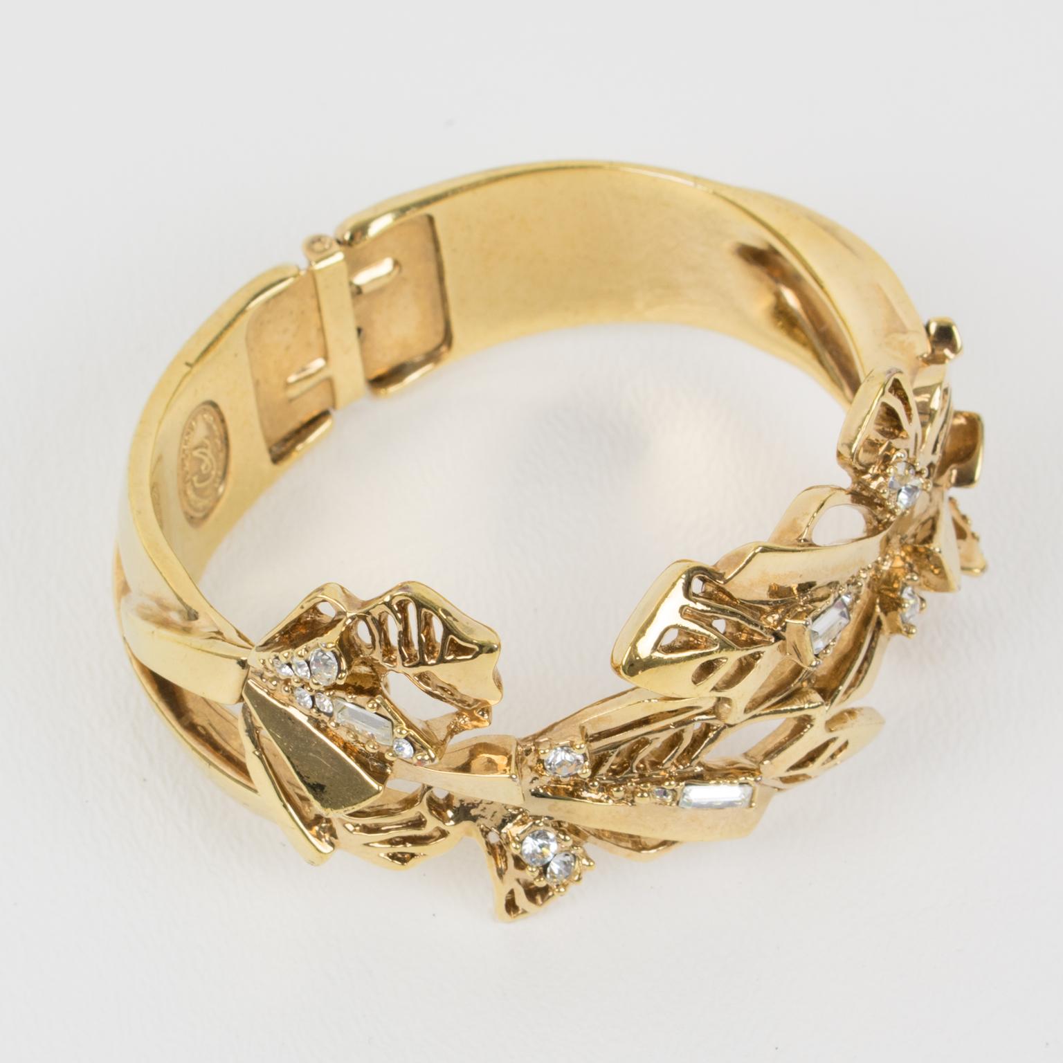 Ce ravissant bracelet à fermoir de Christian Lacroix Paris présente de riches détails ornementaux baroques, avec un motif floral stylisé. L'encadrement en métal doré brillant est sculpté, transparent et orné de strass en cristal de formes assorties.