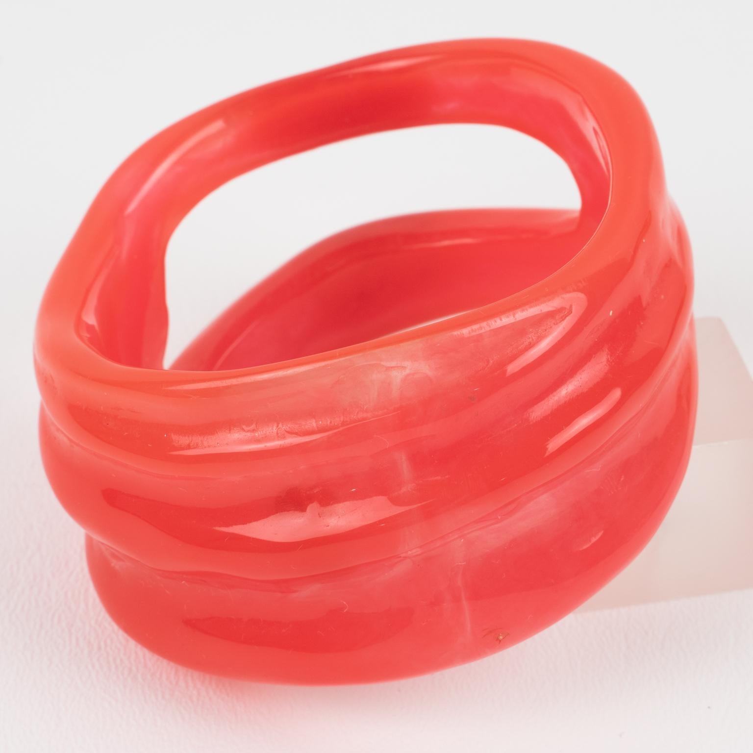 Se trata de una pulsera brazalete maciza futurista de la Era Espacial Christian Lacroix Paris. Tiene un grueso diseño estructural de forma libre y tallado en resina de color rojo rosado sandía con remolinos y transparencias. El interior está firmado