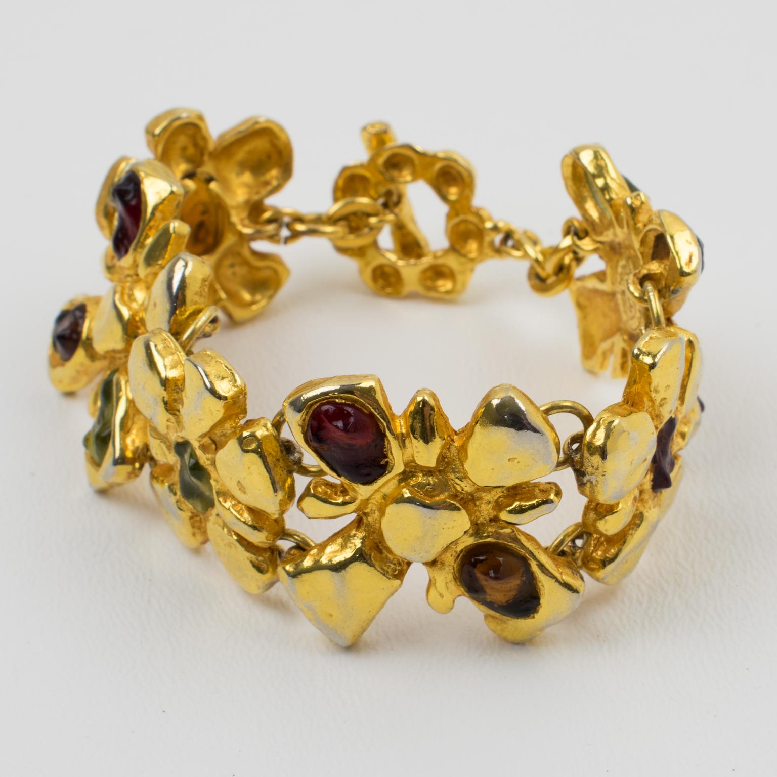 This stunning Christian Lacroix Paris link bracelet features rich ornamental detailing and a stylized floral design. The gilt metal carved and see-thru framing is ornate with Gripoix poured glass rock cabochons in burgundy-red and green pistachio