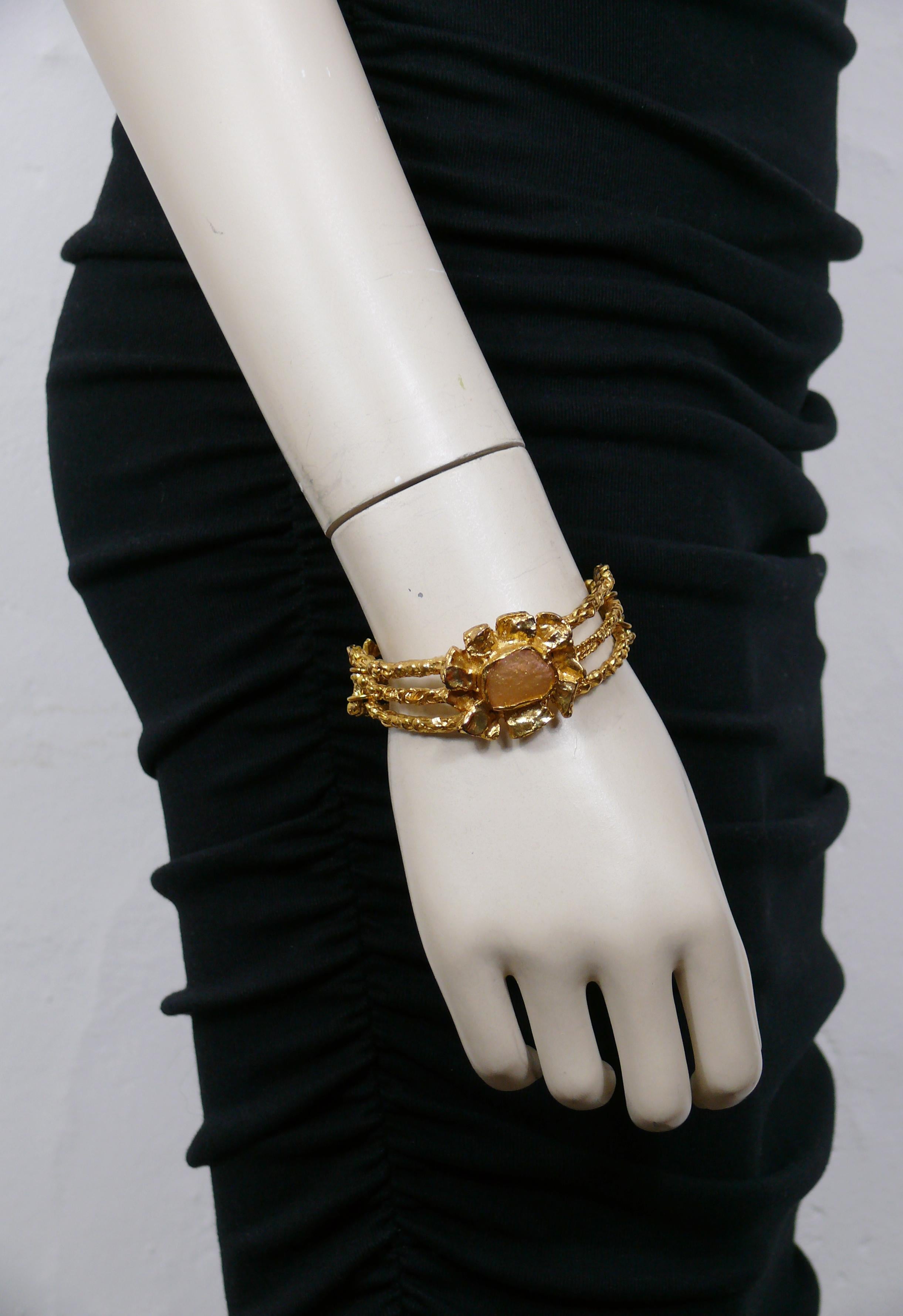 CHRISTIAN LACROIX Vintage-Armband mit goldfarbener Struktur und einer stilisierten Blume in der Mitte, die mit rosa Harz verziert ist.

T-Bügel und Knebelschließe.

Gezeichnet CHRISTIAN LACROIX CL Made in France.

Ungefähre Maße: Umfang ca. 17,28 cm