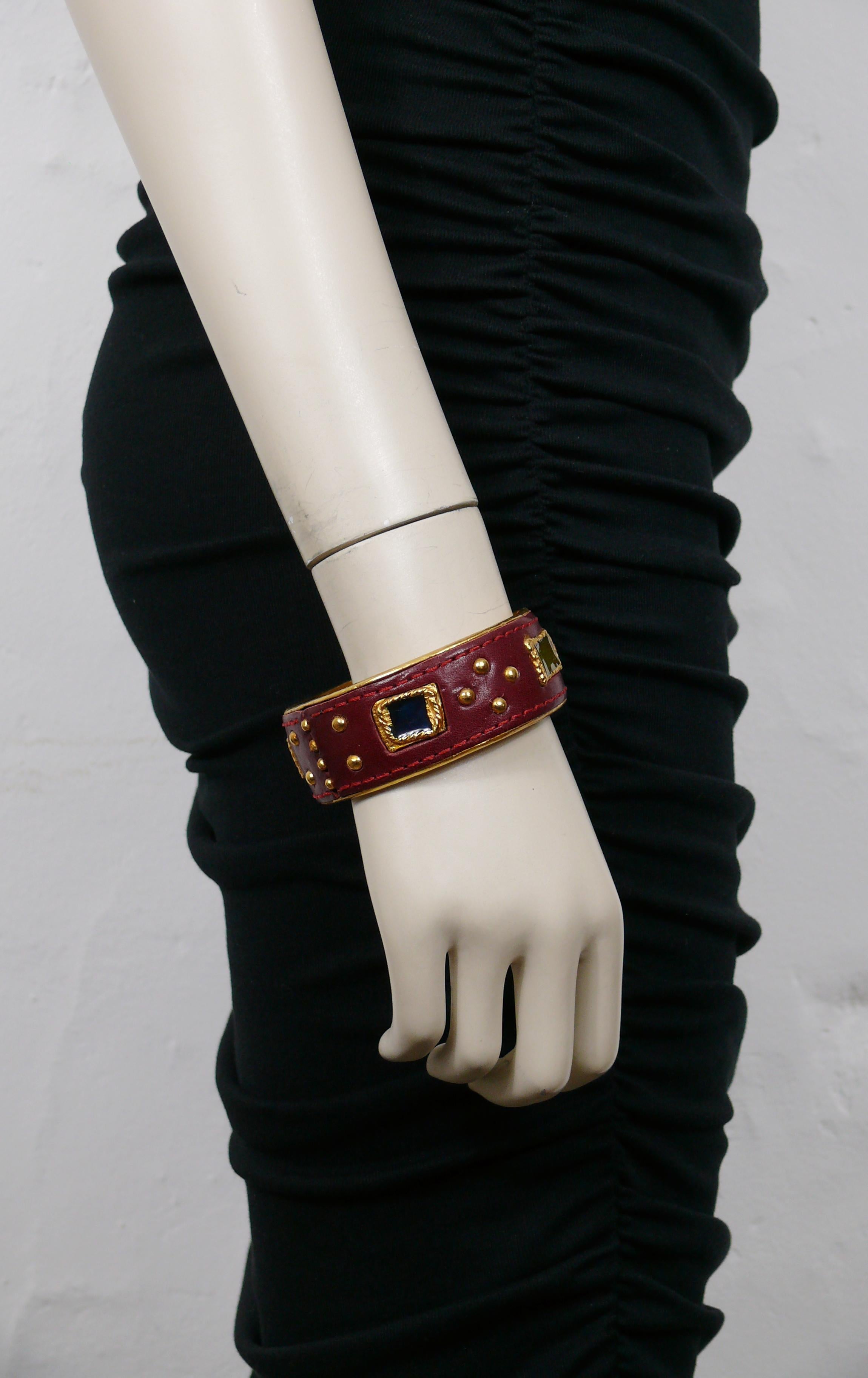 CHRISTIAN LACROIX Vintage-Armband in Goldton mit burgunderrotem Leder mit Sattelnaht, verziert mit Nieten und gegossenen Harz-Cabochons.

Gezeichnet CHRISTIAN LACROIX CL Made in France.

Ungefähre Maße: Innenumfang ca. 20,11 cm (7,92 Zoll) / Breite