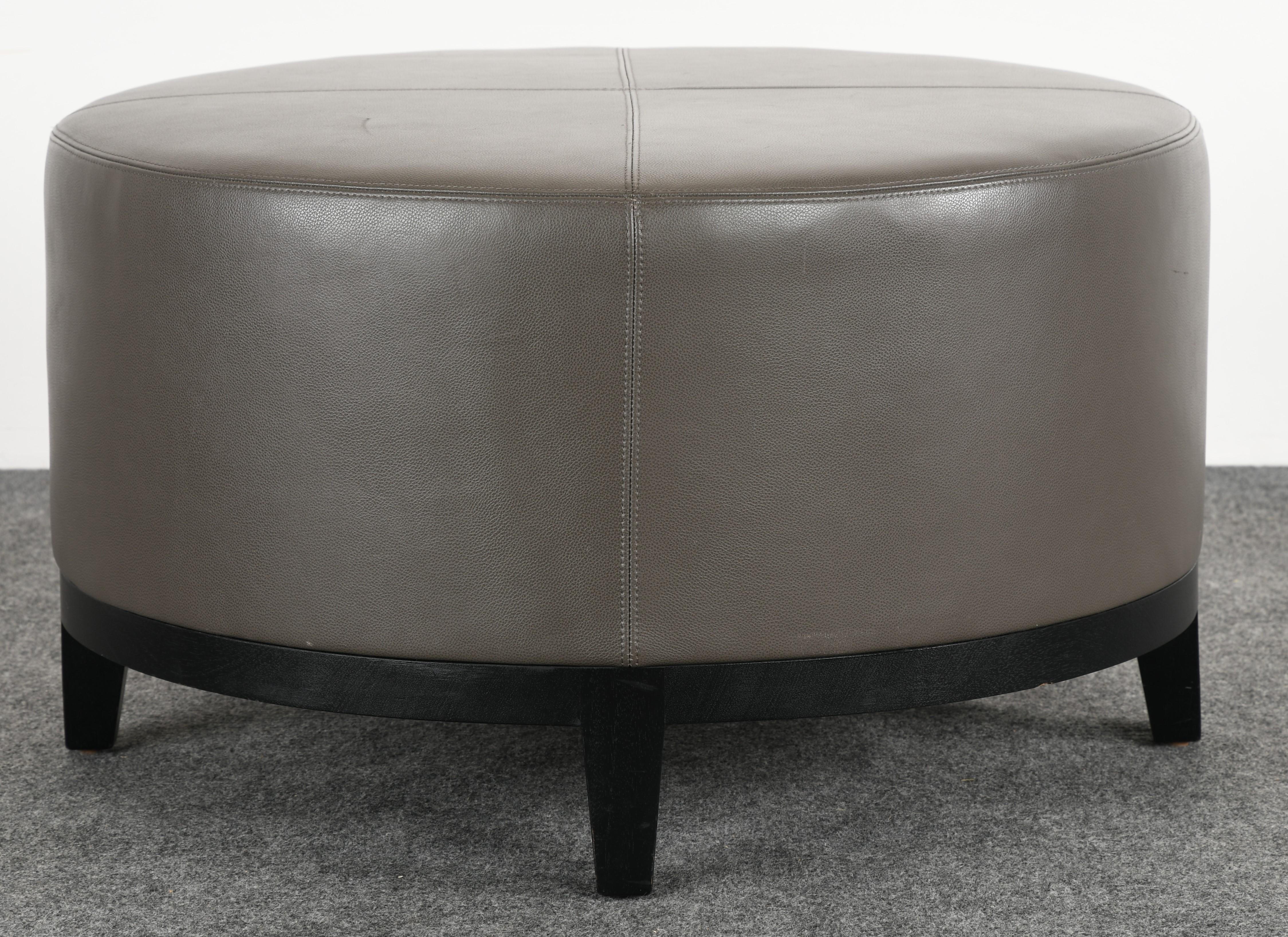 A luxurious Christian Liaigre round ottoman, bench, or pouf for Holly Hunt. Upholstered in high-end grey leather on an ebonized oak base. The bench is in very good condition and structurally sound with minor scuffs to the leather, as shown in the