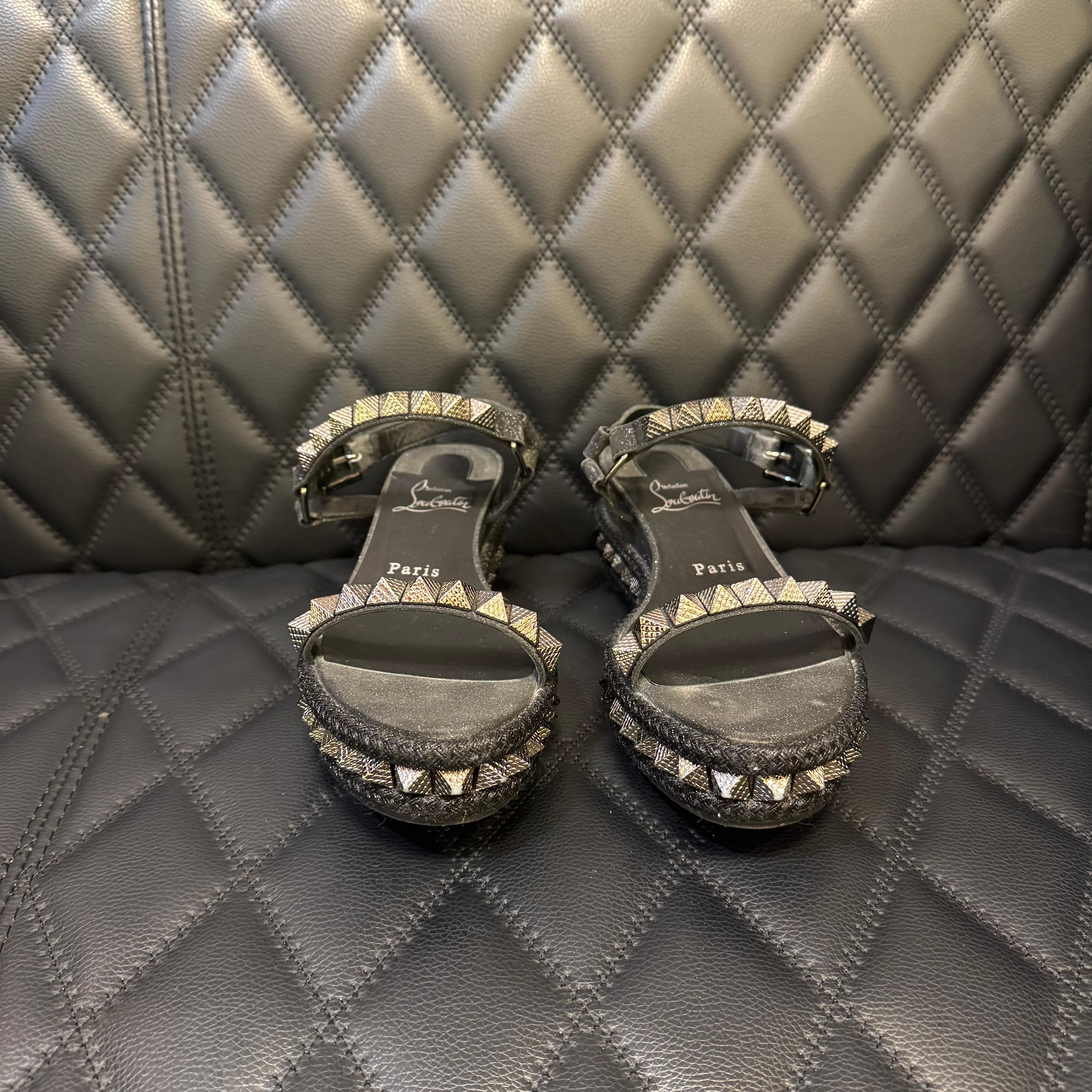 Louboutin pyraclou 60 en noir pailleté. En très bon état, à peine usé. Petites éraflures sur la doublure du bracelet en cuir. Un protecteur de semelle est appliqué sur les semelles inférieures. Livré avec sac à poussière, boîte et reçu d'origine.