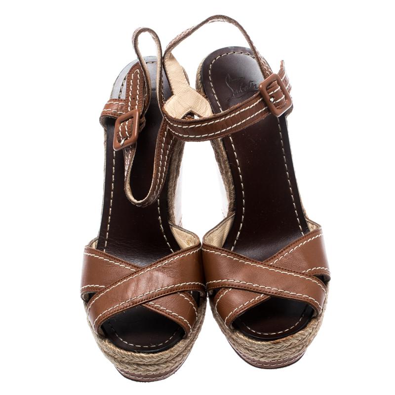 Set on a towering wedge heel, these sandals from the house of Christian Louboutin features a brown leather body with cross strap on the front. It comes with an ankle strap closure, espadrille detailing on the midsoles and highlighted with contrast