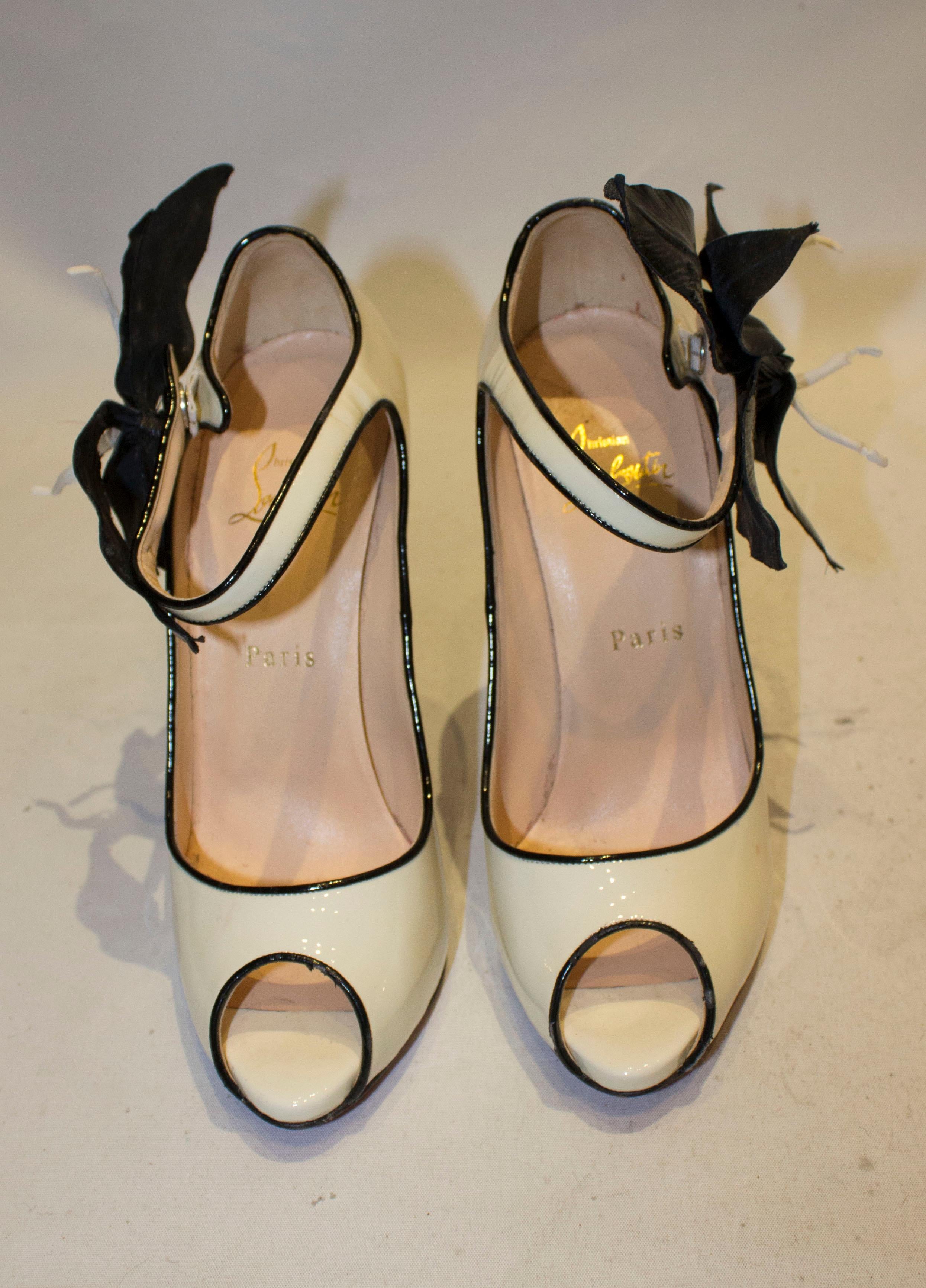 A fun pair of shoes by Christian Louboutin,in patent cream leather with a black trim. The shoes have a peep toe, hidden platform, and ankle strap with popper detail and flower decoration. Size 38 , heel height 5''.