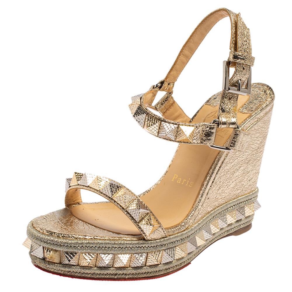Christian Louboutin's craftsmanship in shoemaking is exemplified in these stunning sandals. They have been crafted from foil leather in a gold shade and feature pyramid studs then elevated on 10 cm wedge heels supported by platforms.


