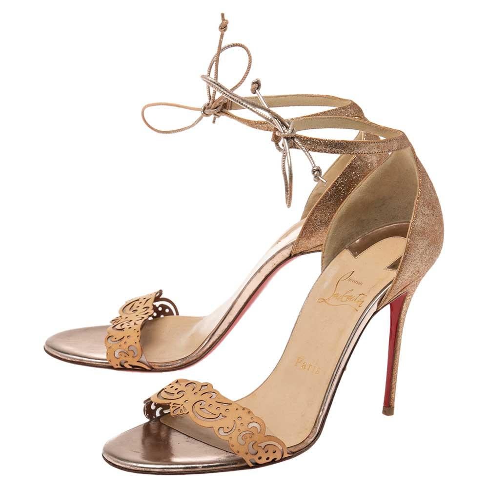 Introduce bold sophistication to your closet with these stunning sandals from Christian Louboutin. Doused in tan and gold hues, these sandals are rendered in leather and glitter with laser-cut vamp straps, ankle tie-ups, and 10.5 cm stiletto heels.