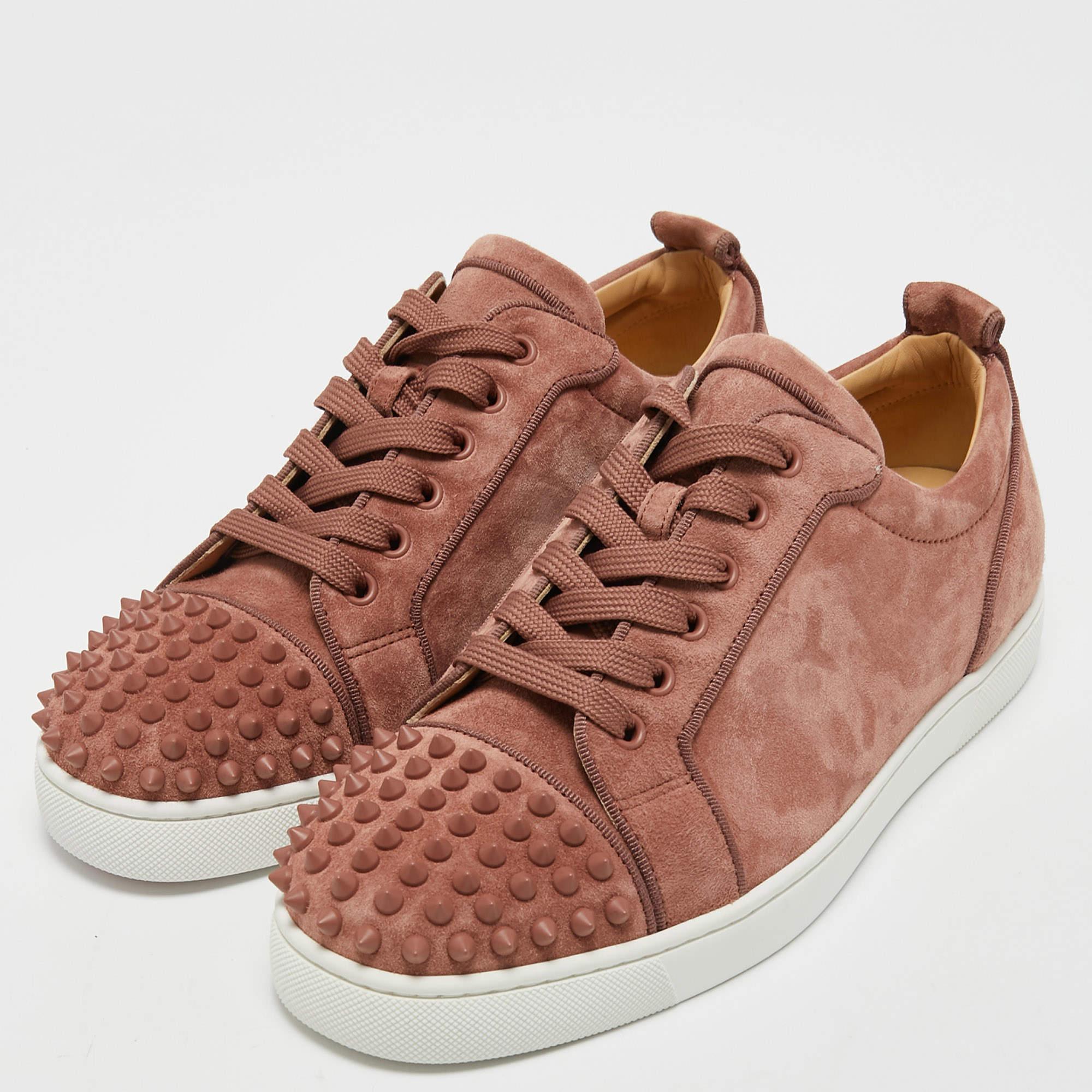 The Christian Louboutin Louis Junior sneakers are luxurious and edgy footwear. Made from premium light pink suede, they boast a low-top design with iconic red rubber soles. The sneakers are adorned with signature spikes, adding a bold and