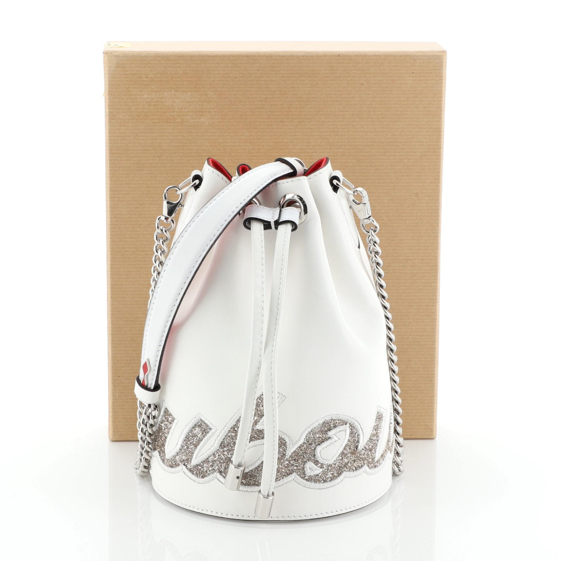 This Christian Louboutin Marie Jane Bucket Bag Leather Medium, crafted in white leather, features chain-link and leather strap, signature Louboutin logo in frosted glitter and silver-tone hardware. Its drawstring closure opens to a red fabric