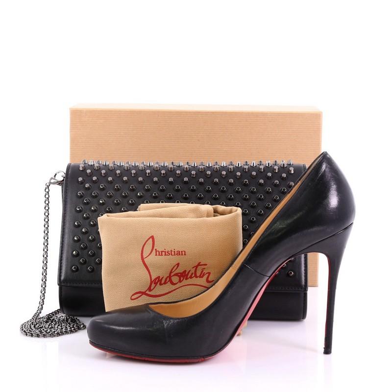 This Christian Louboutin Paloma Clutch Spiked Leather, crafted in black leather, features spiked studs at front flap, chain-link shoulder strap, and gunmetal-tone hardware. Its magnetic snap button closure opens to a red leather interior with