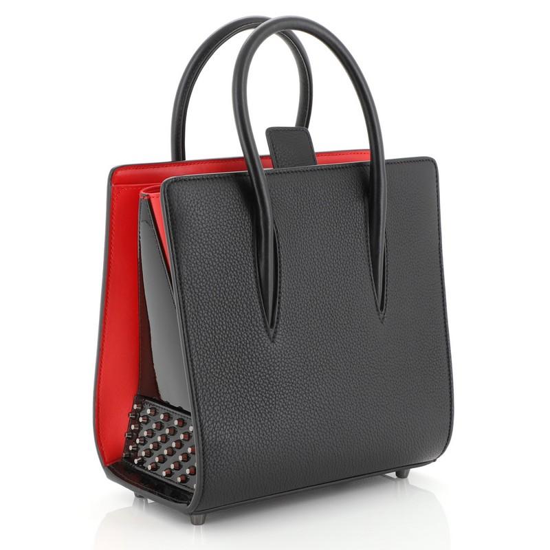 This Christian Louboutin Paloma Tote Leather Small, crafted in black leather, features dual rolled leather handles, spiked patent leather on the sides, protective base studs, and gunmetal-tone hardware. Its tab closure opens to a red leather