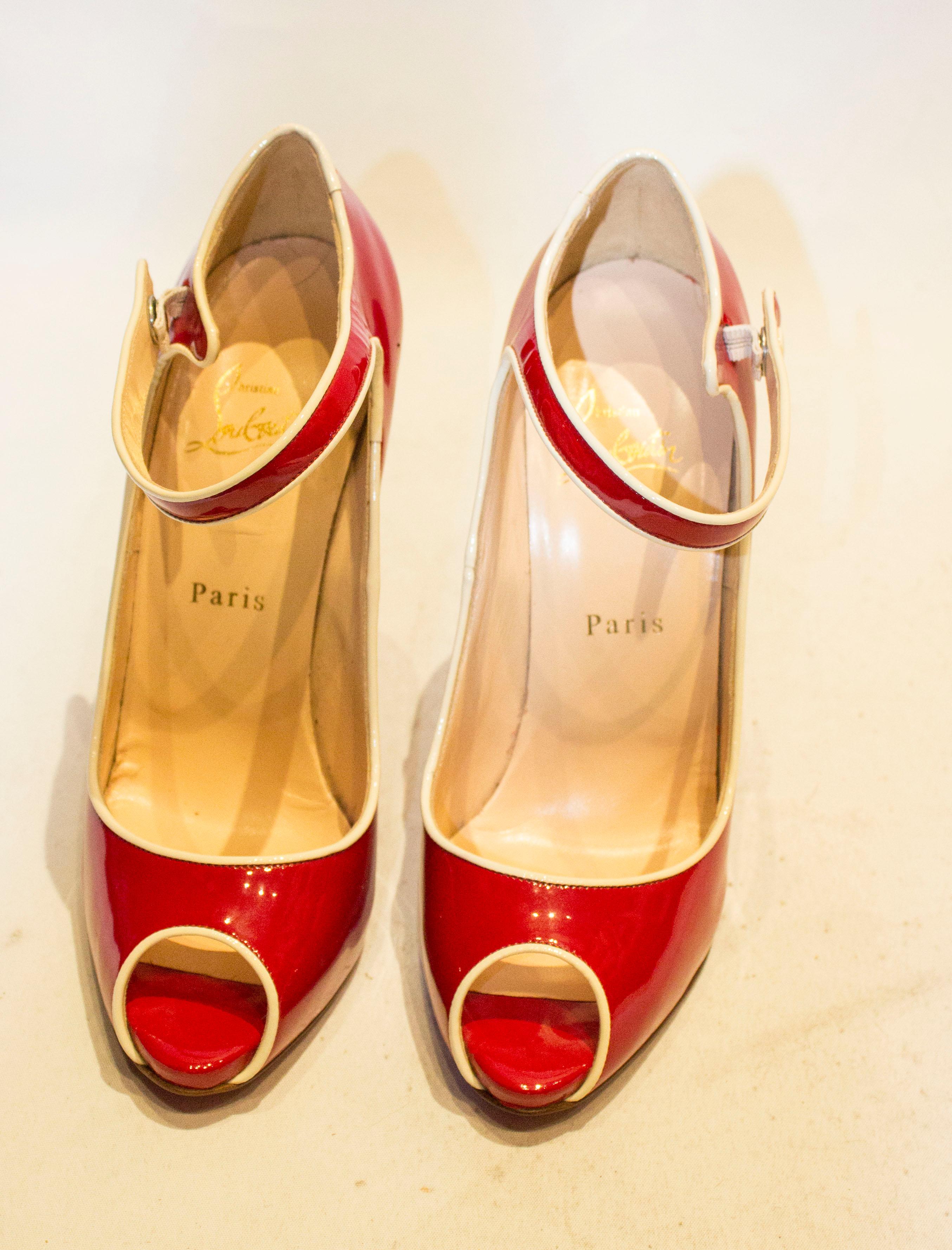 A fund pair of shoes by Christian Louboutin . The shoes are in red patent leather with a cream trim, peep toes and ankle strap. Size 38'', heel height 5''.