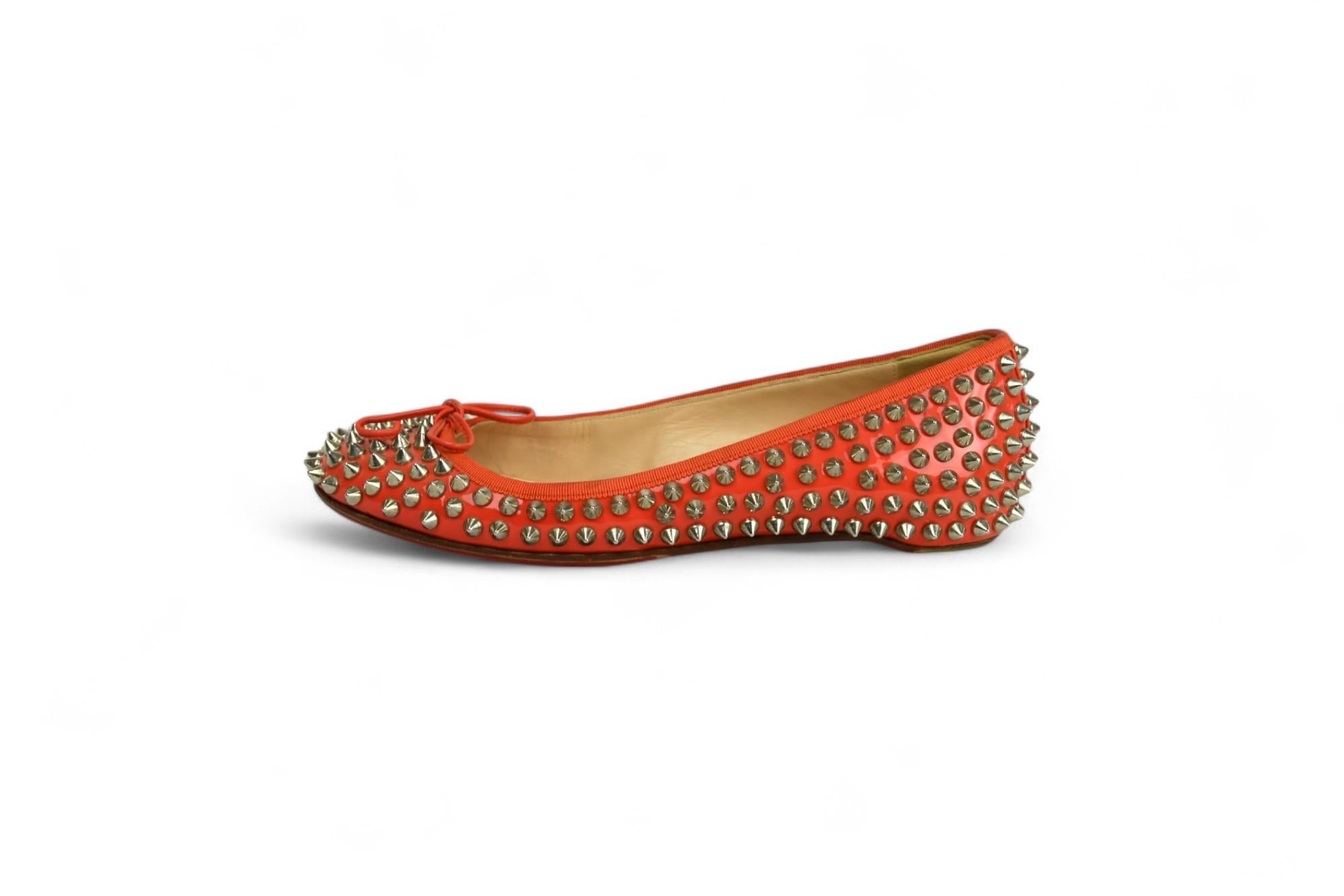 Ces ballerines cloutées Christian Louboutin, réalisées en cuir verni rouge brillant et ornées de pointes argentées sur tout le pourtour, sont à la fois élégantes et emblématiques. Un nœud féminin sur l'empeigne contraste avec l'ornementation