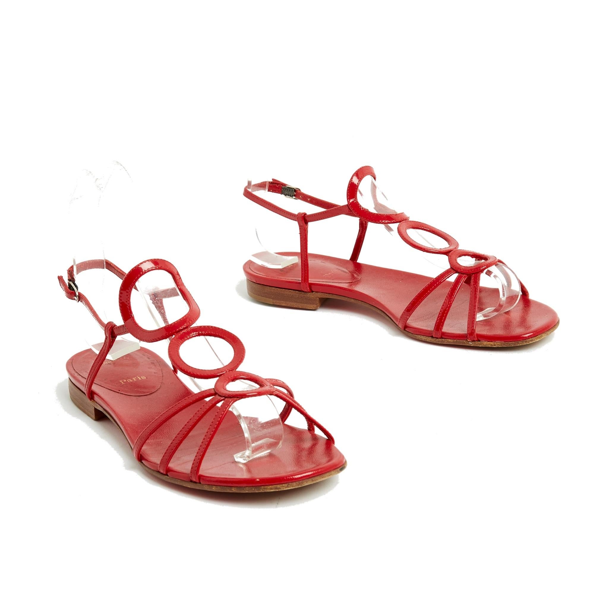 Sandales plates Christian Louboutin modèle Aplarona en cuir verni rouge avec fines lanières en forme de cercle sur le dessus du pied. Taille EU37.5 ou UK 4.5 et US7. Les sandales ont été portées mais seule la semelle est marquée. Elles sont