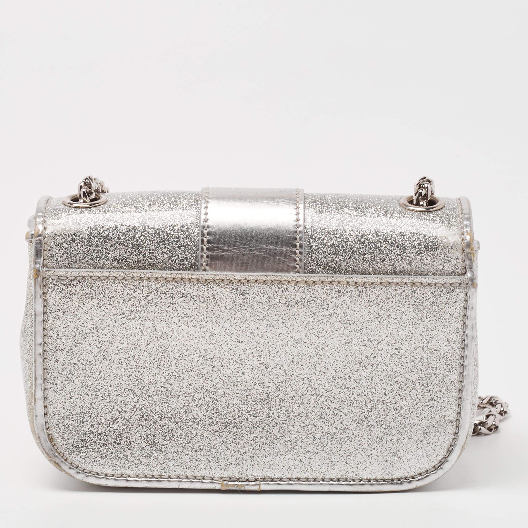 This modern and edgy Sweet Charity bag is from Christian Louboutin. Crafted from silver patent leather, the bag comes with eye-catching spike embellishments and signature Loubi bow detail. The insides are fabric-lined and the bag is complete with a
