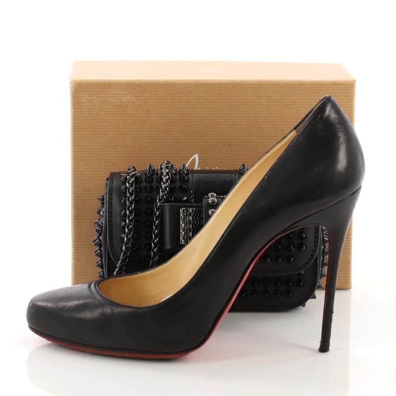 This Christian Louboutin Sweet Charity Crossbody Bag Spiked Leather Mini, crafted from black spiked leather, features a long chain strap, Louboutin red sole decor, mesh bow design, and gunmetal-tone hardware. Its hidden magnetic snap closure opens