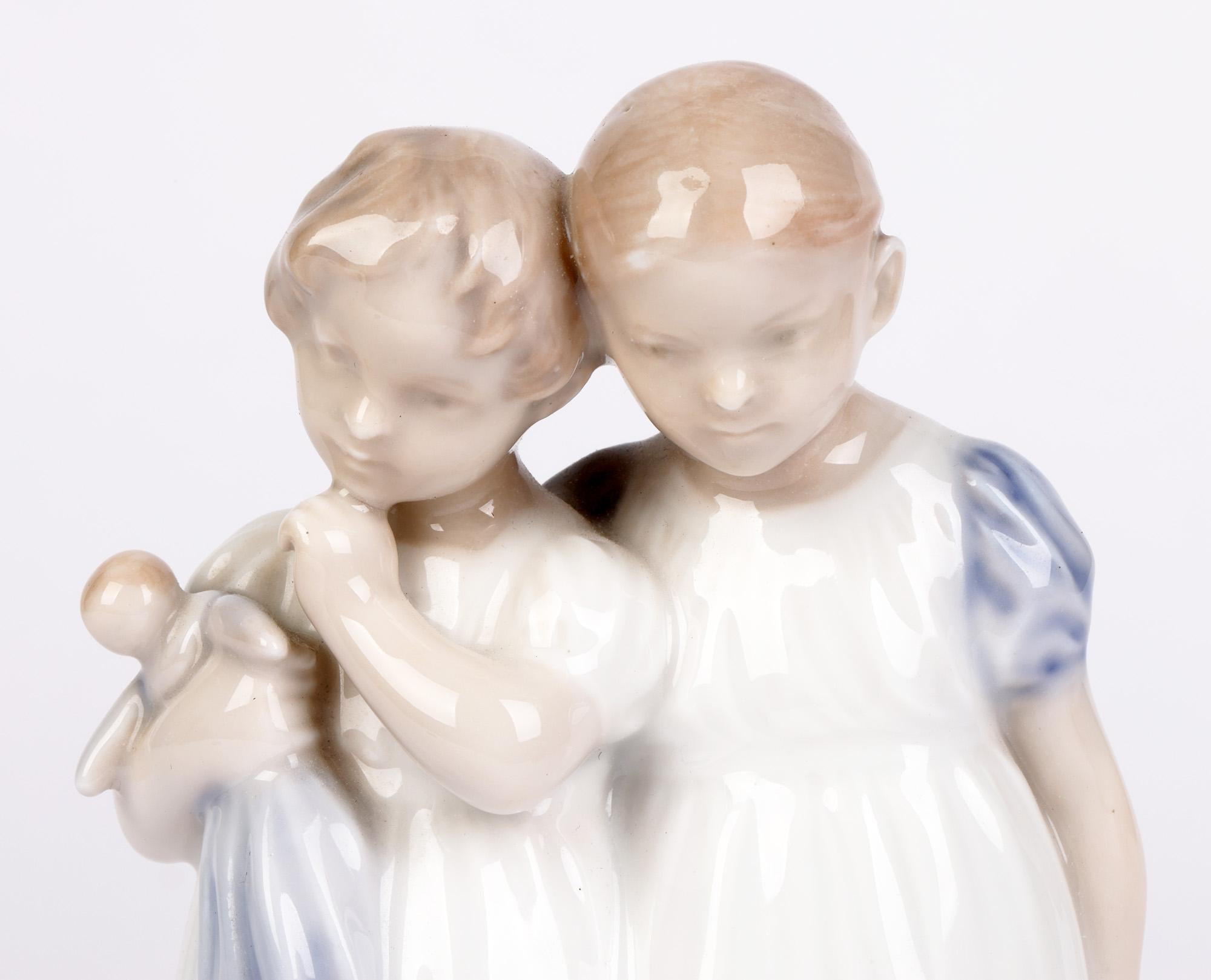 A scarce Danish Royal Copenhagen porcelain figure of two girls with a doll designed by Christian Thomsen (1860-1921) and dating from the mid 20th century. The figure stands raised on a small rounded base and portrays two girls dressed in night gowns