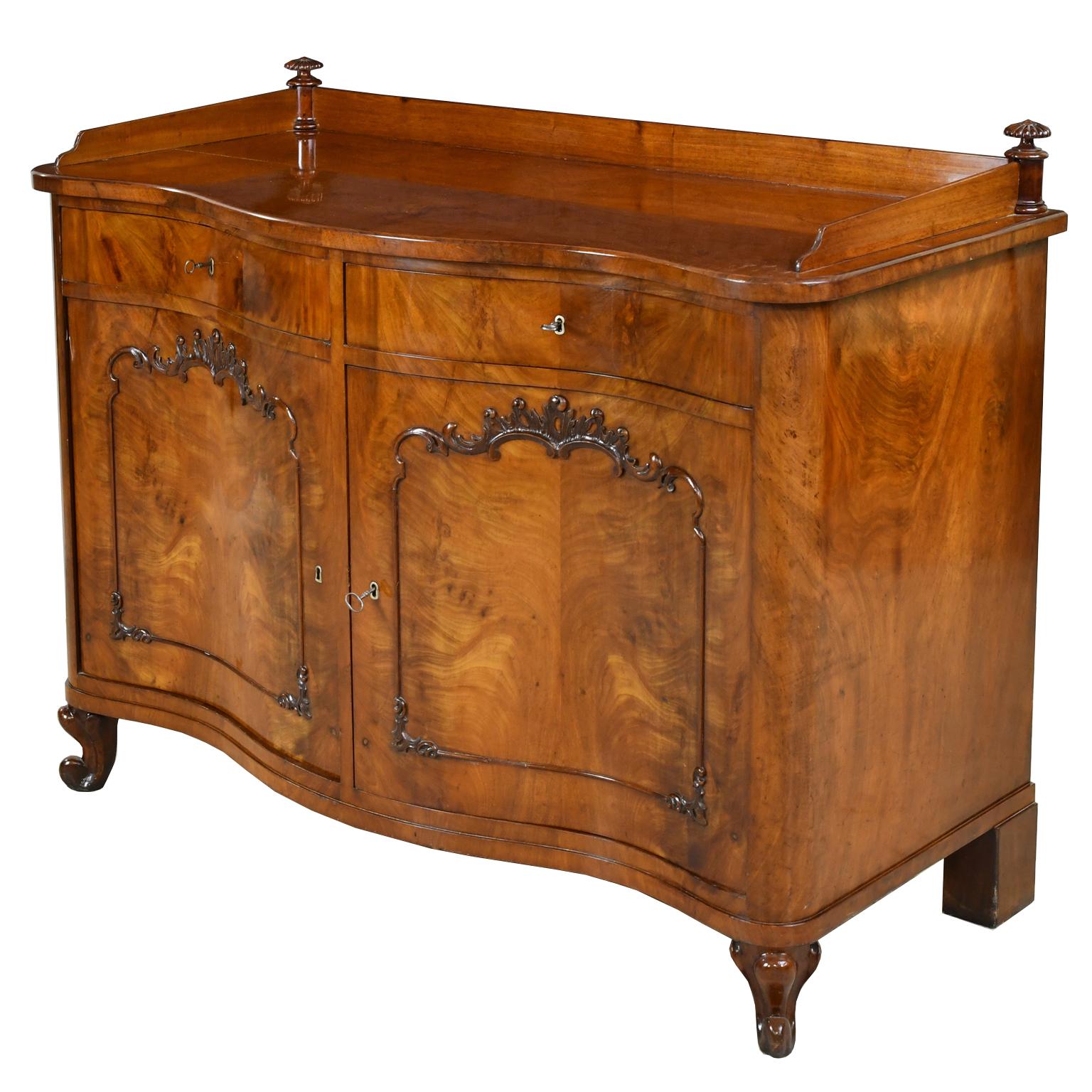 A very lovely and well-crafted sideboard/ credenza in fine West Indies mahogany with serpentine front that features two drawers over two cabinet doors, with carved rocaille details bordering the door panels. A small backsplash runs along the top
