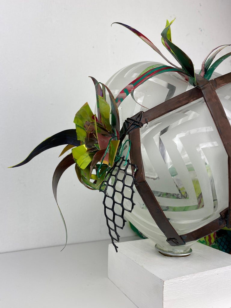 Flirt & Divert, is a part of a series of contemporary blown glass mixed media botanical plant sculptures. This one dangles off an edge while sitting upon a magnetized base and has a hand created design sandblasted onto the surface. Made from