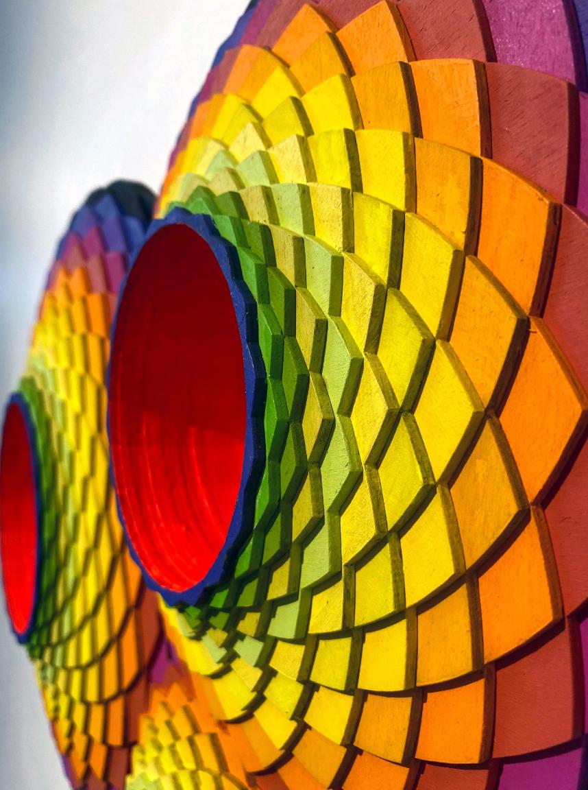 Il TriVortex di Christine Romanell è un'ipnotica costruzione in acrilico su legno tagliato al laser che fonde geometria sacra, illusione ottica e vibrante teoria del colore in una dinamica forma tridimensionale. I modelli stratificati e