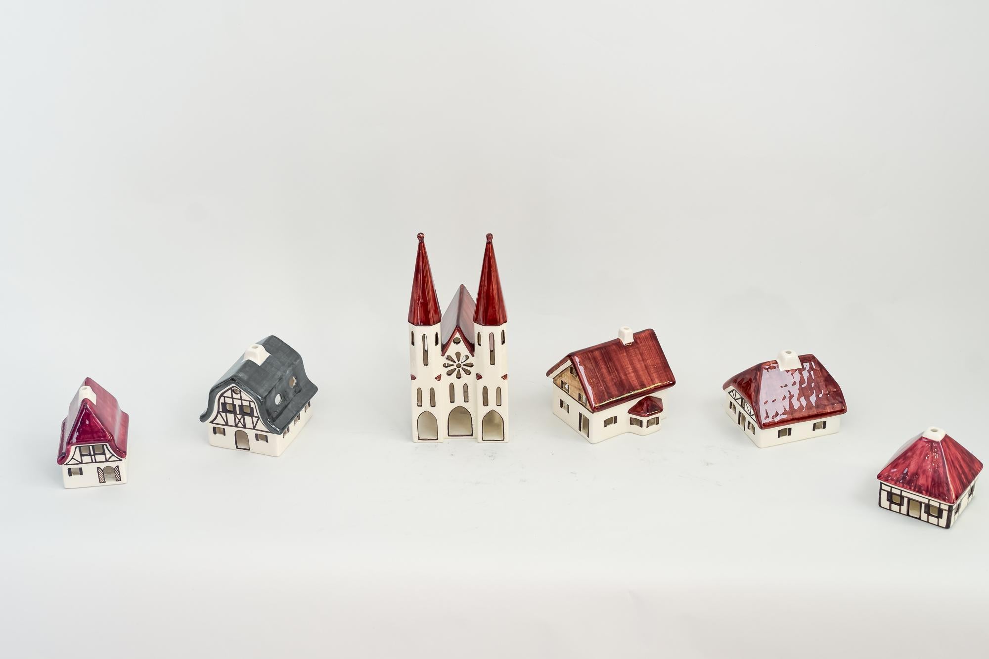 Handcrafted Christmas ceramic houses for candle light deco in shape of a village around 1970s

The church dimensions are: 
Hight: 25cm
Wide: 11cm
Deep: 16cm

All others are around : 
Hight: 11 cm
Wide: 10 cm
Deep: 11 cm.