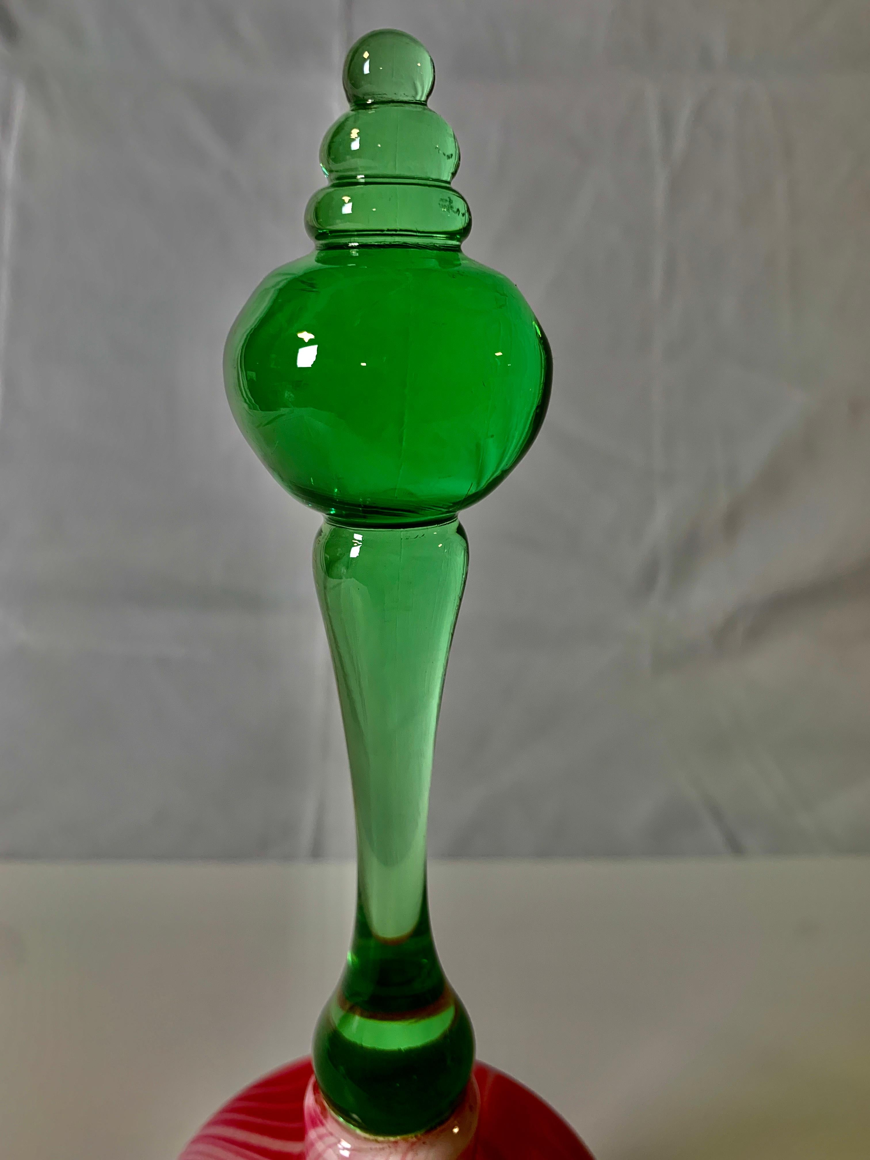 This bell is red and white with a green handle. It is perfect for Christmas.
Made in the Nailsea glassworks in England circa 1840 the blown glass is colored with red and white marbling and is elegantly shaped. It has an exquisite forest green glass